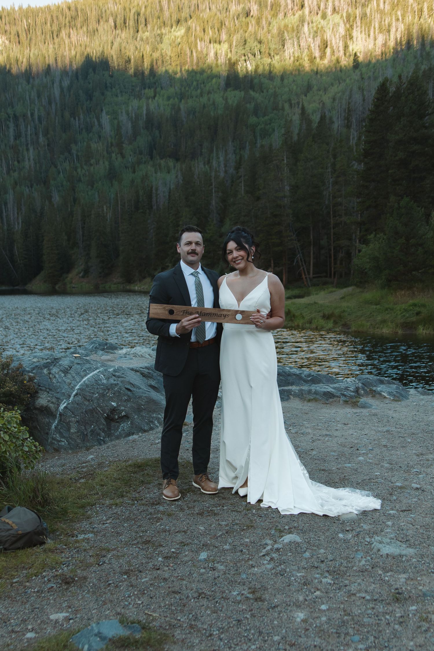 A lakeside wedding ceremony unfolds against a backdrop of evergreen forest and mountain scenery.