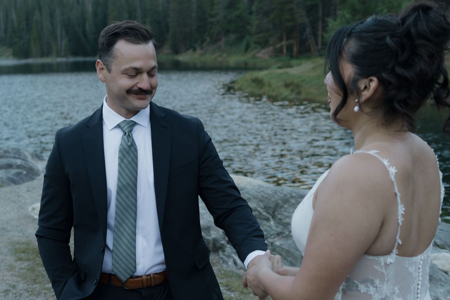 Newlywed couple shares intimate moment near lake while photographer captures wedding portraits.