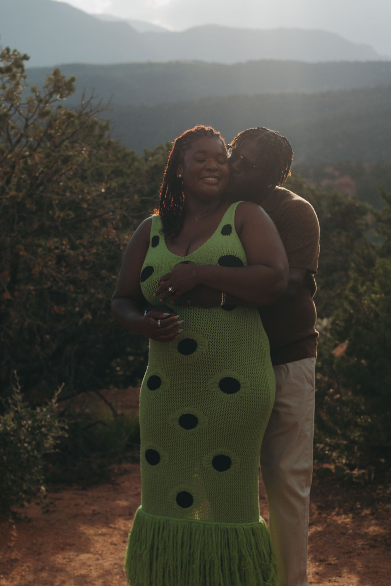 A romantic couple shares a tender moment against a backdrop of misty mountains at sunset.