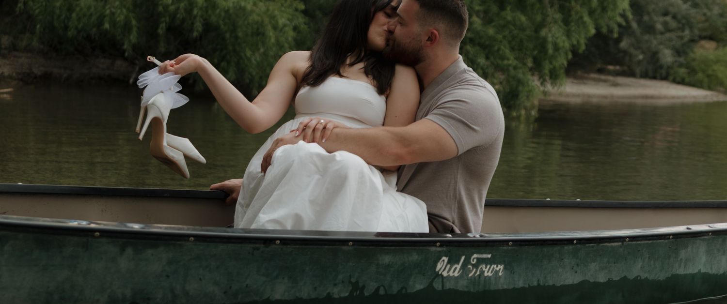 Romantic wedding couple embraces while rowing in a classic wooden boat across a tranquil lake.