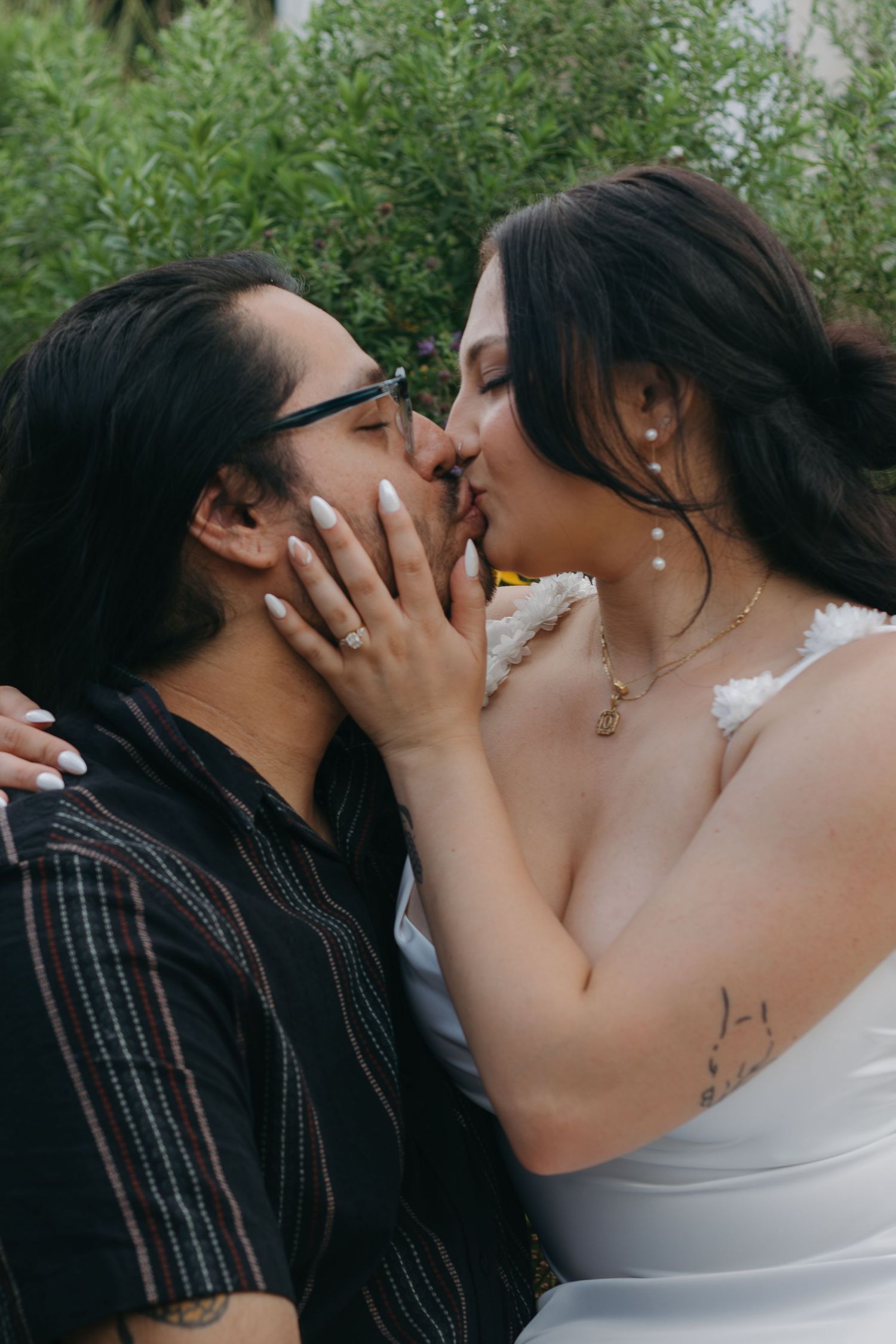 An intimate moment captured between a couple surrounded by green foliage.