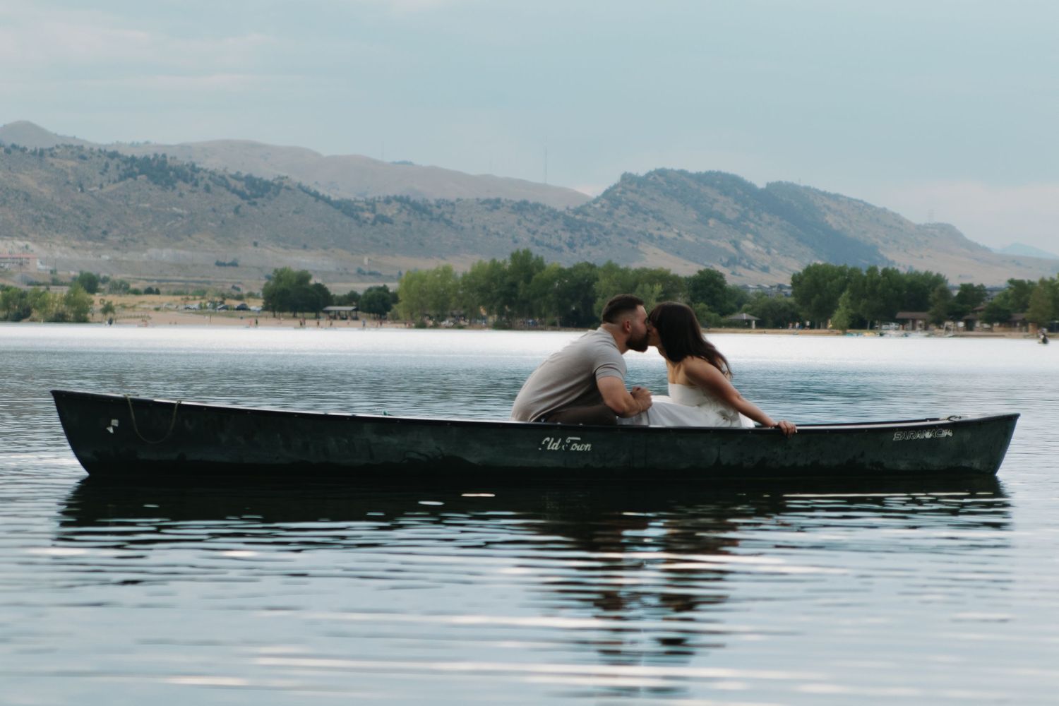 A couple share a tender kiss while canoeing together on a serene mountain lake.