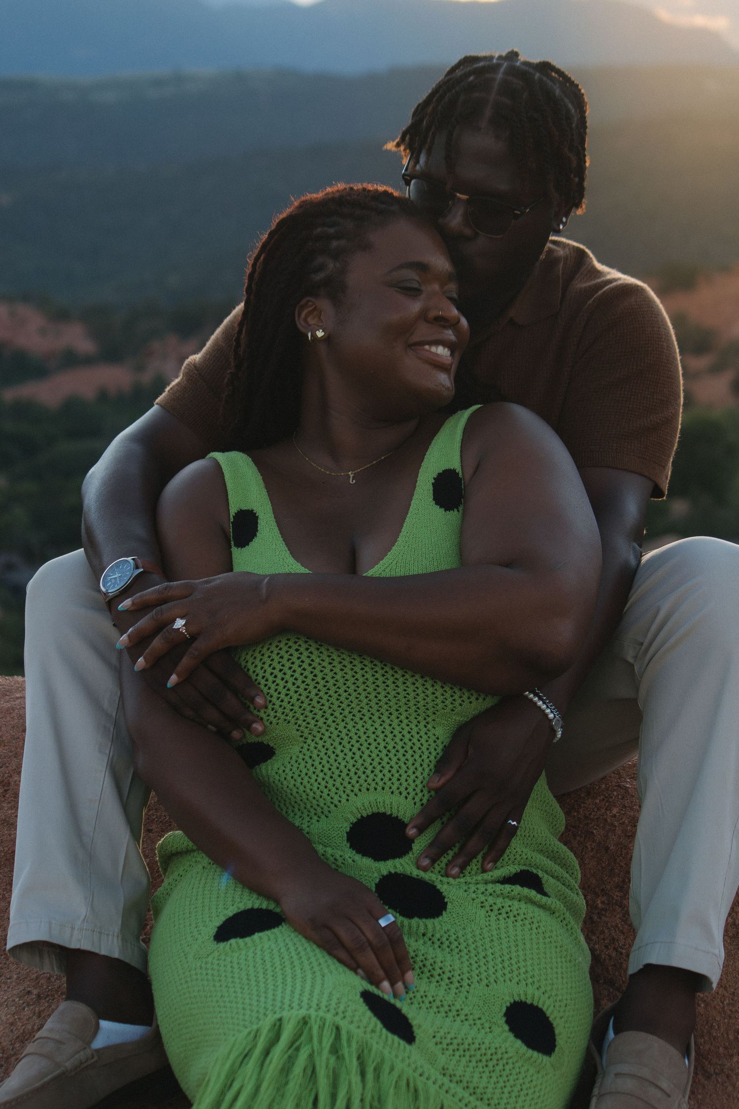 A tender moment captured at sunset with mountains in the background and a bright green polka dot dress.