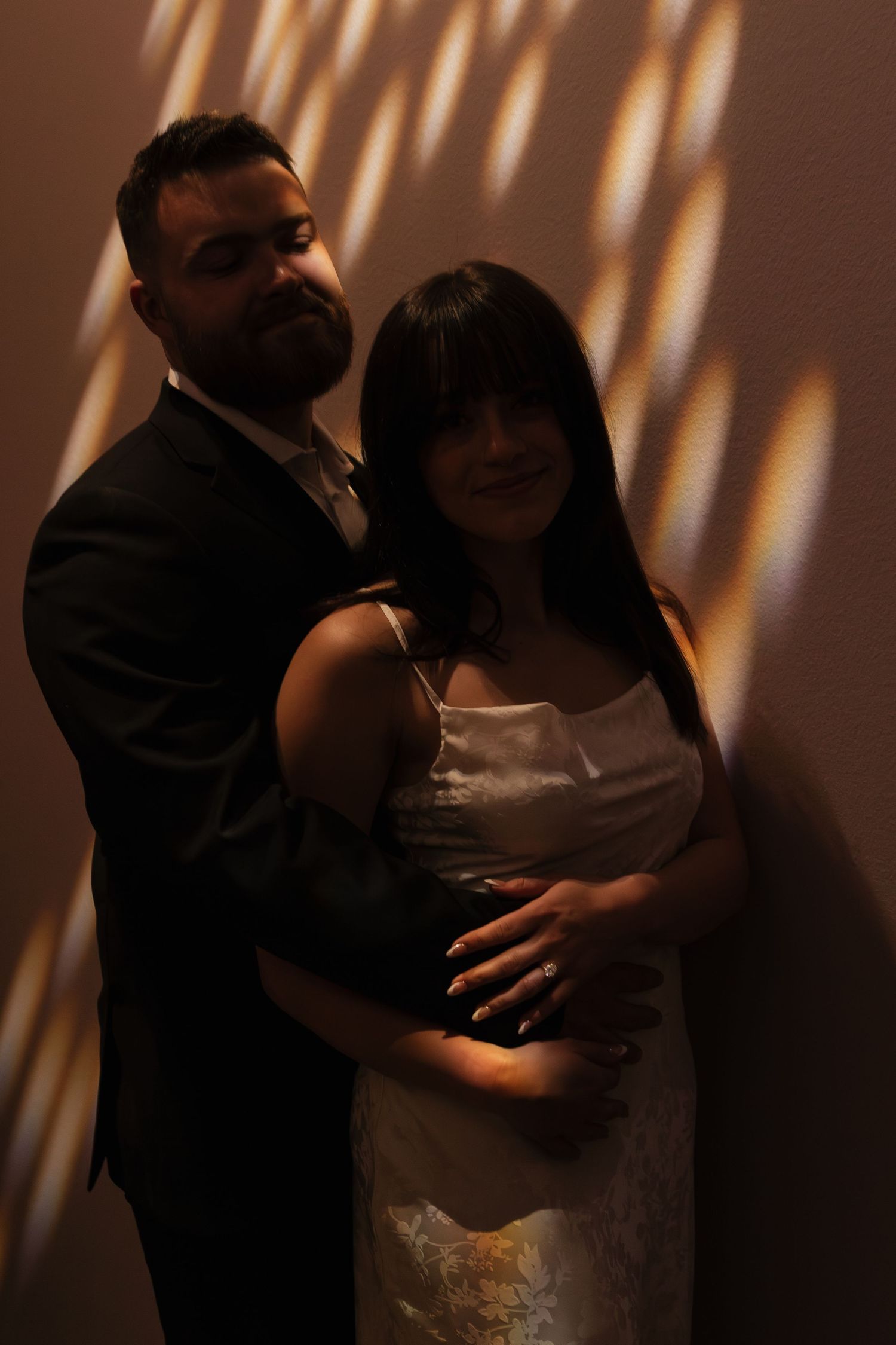 Couple dancing in dramatic lighting with shadows cast on wall behind them creating artistic silhouettes.