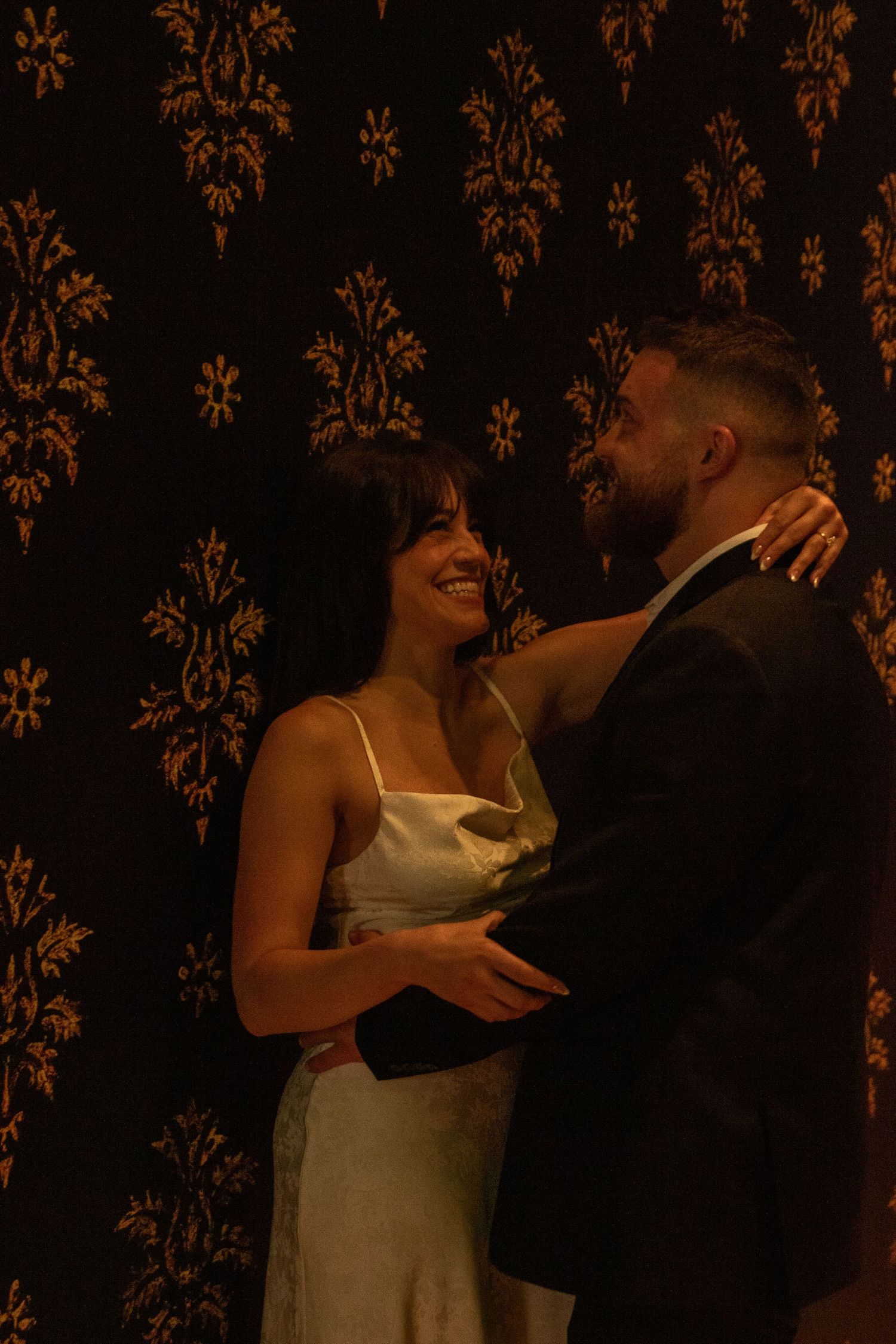 Couple sharing tender moment against dark floral wallpaper background.
