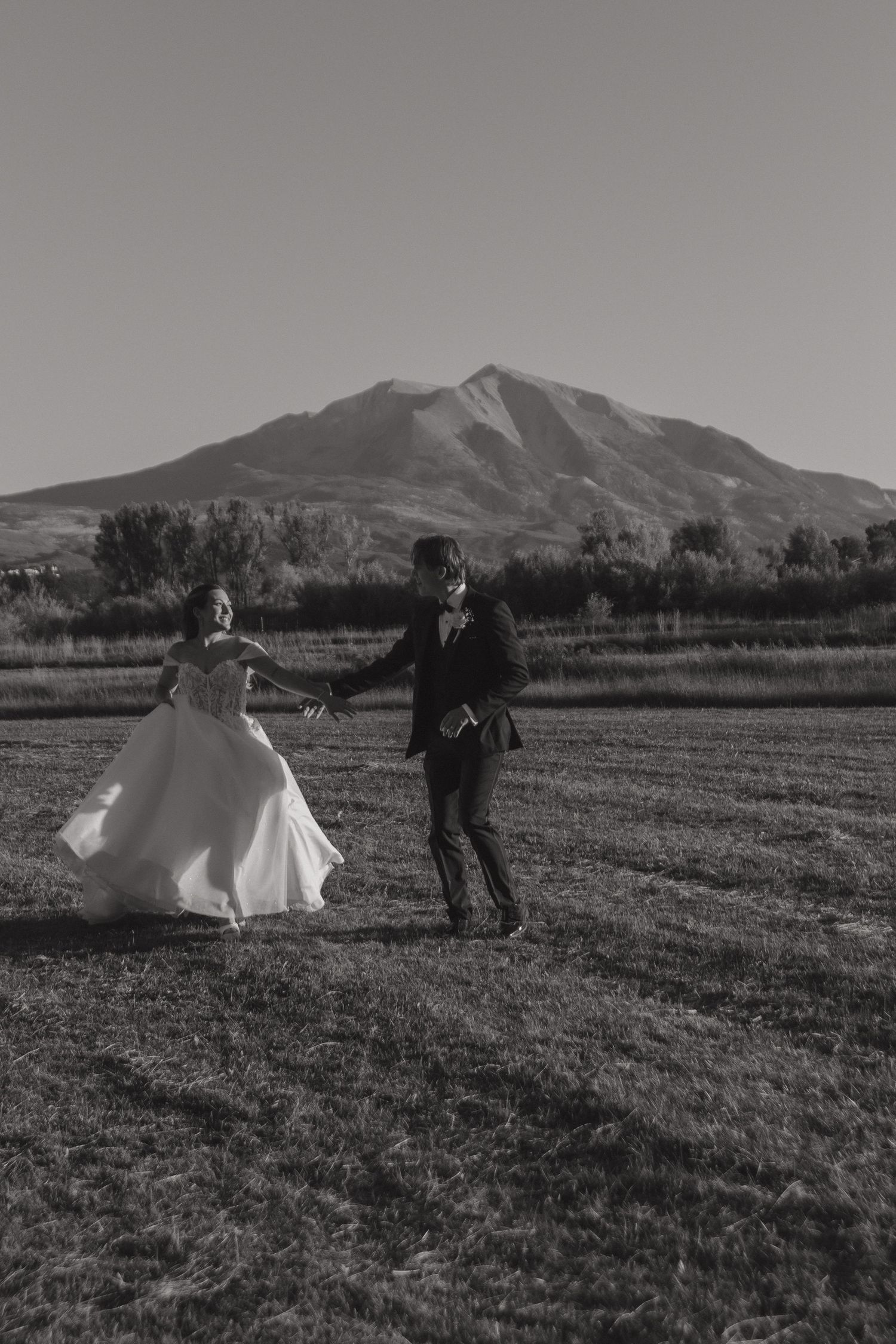 Black and white sequence of couple running playfully in field with mountain backdrop.