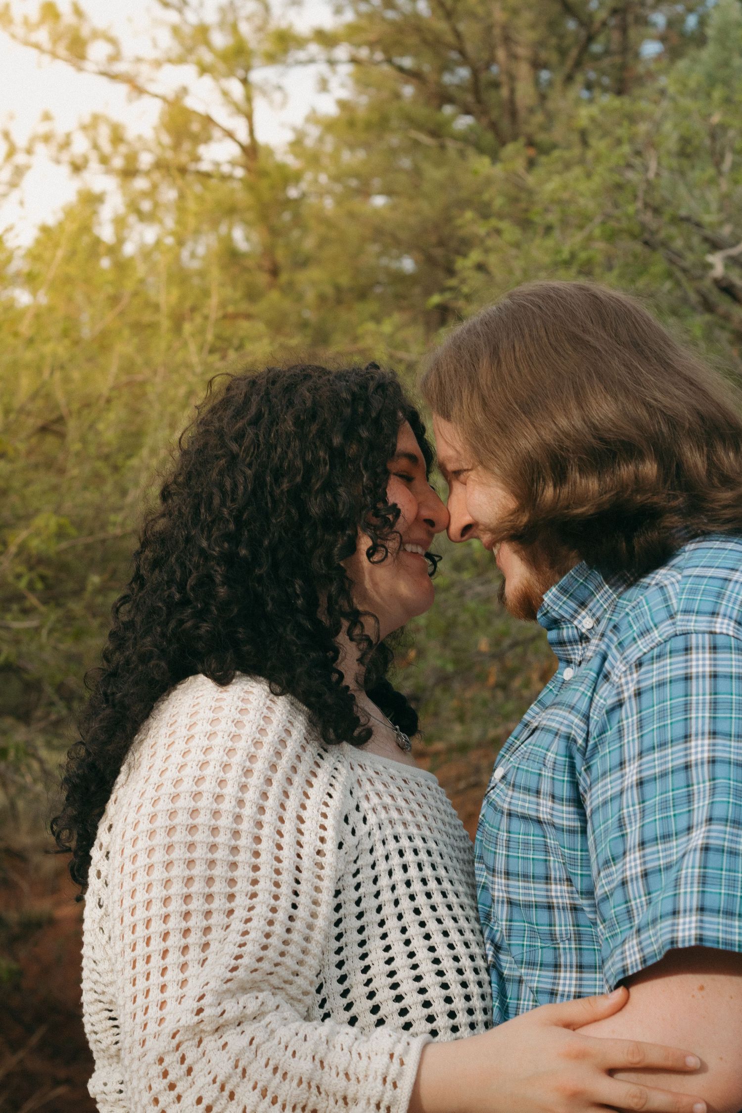 Romantic close-up of couple sharing tender moment on sunny nature trail.