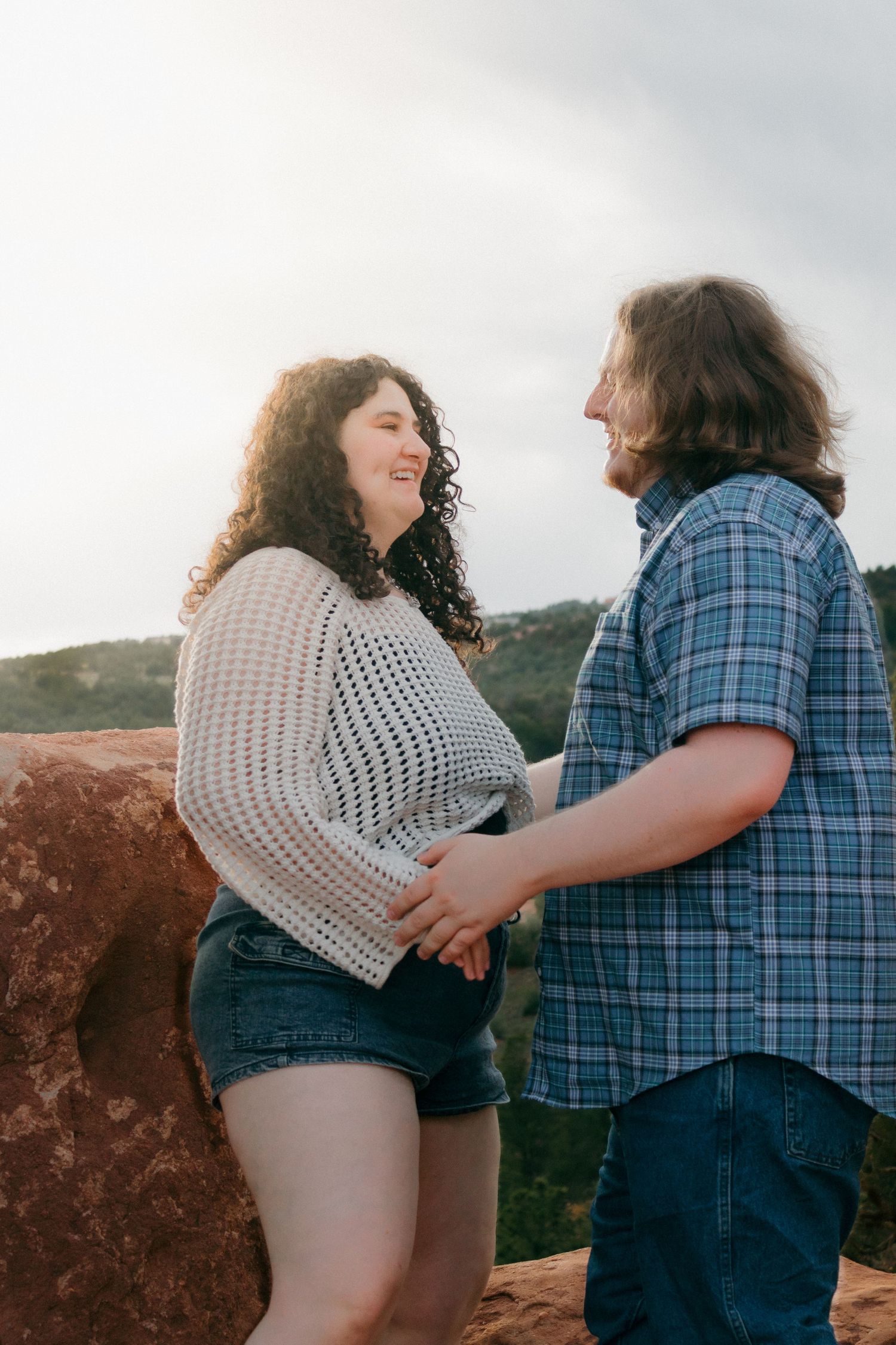 A couple embracing and laughing together on red rocks with a mountain landscape behind them.