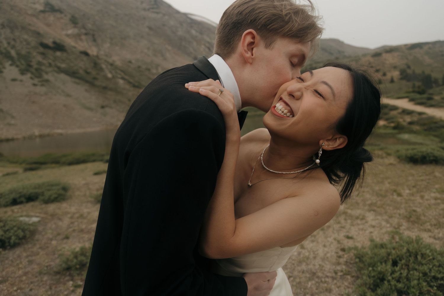 Bride laughing joyfully as groom kisses her cheek during mountain wedding elopement photo session.