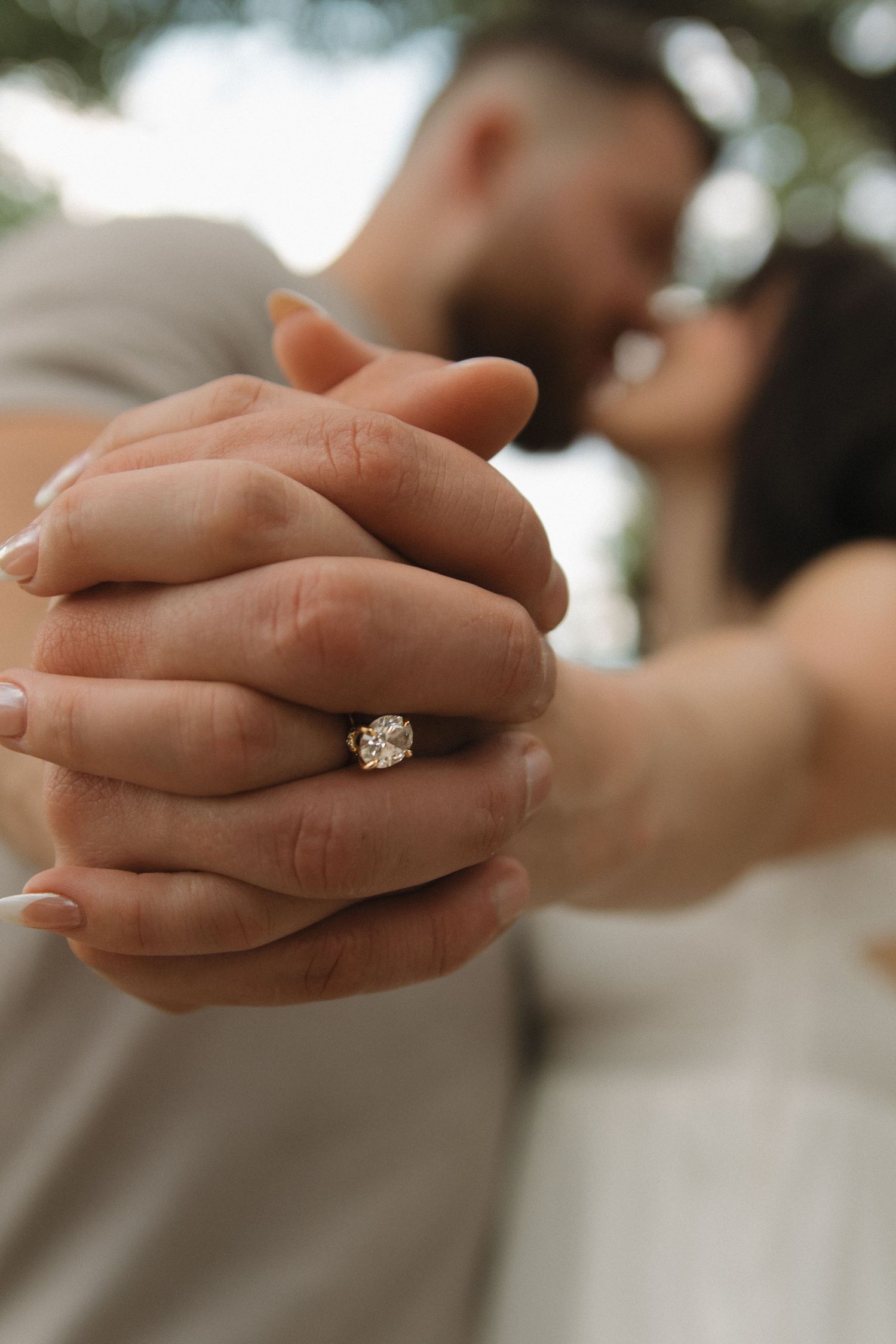 Close-up shot of hands with an engagement ring reflecting soft natural light.