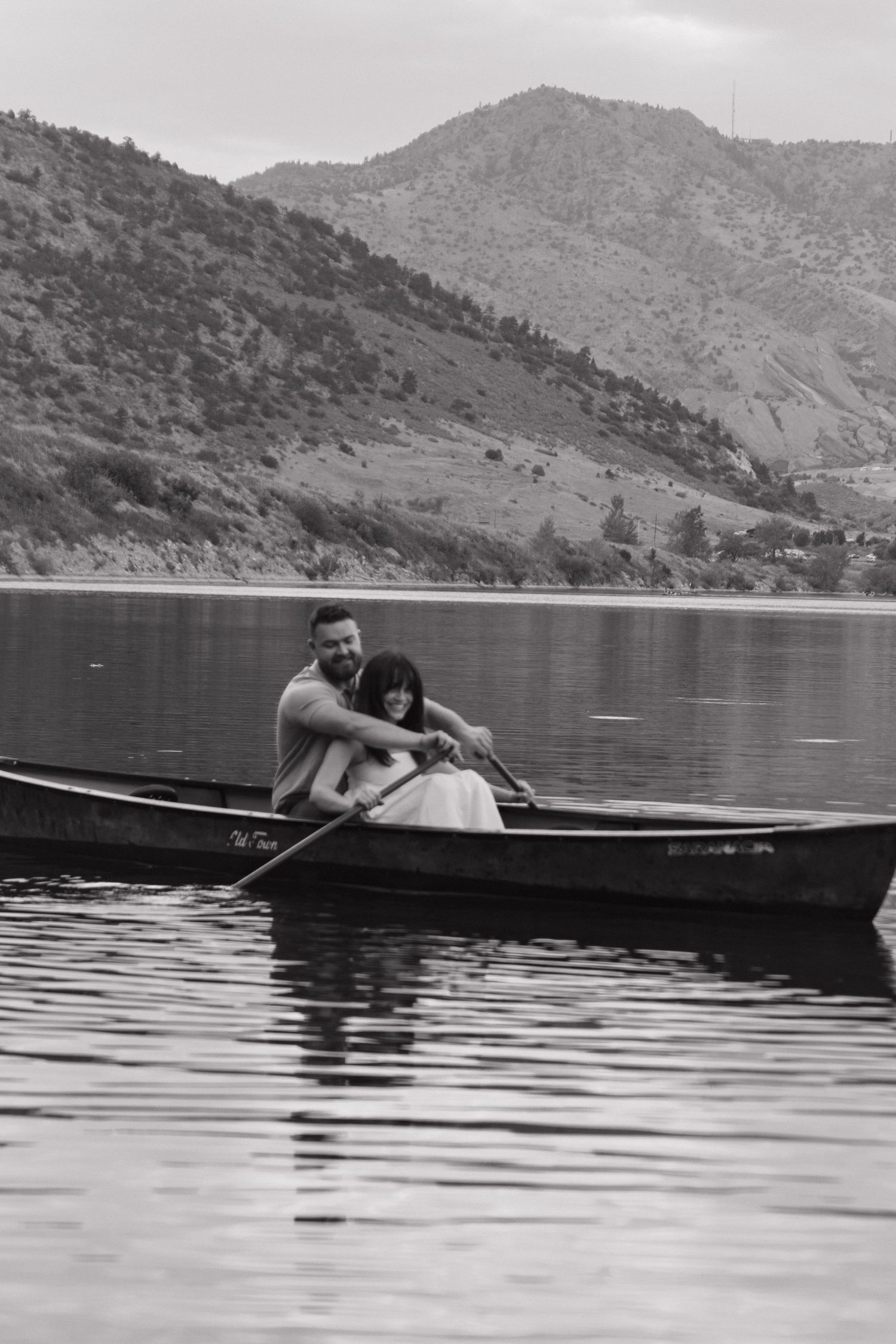 A serene black and white photograph of a boat floating on a mountain lake with hills in the distance.