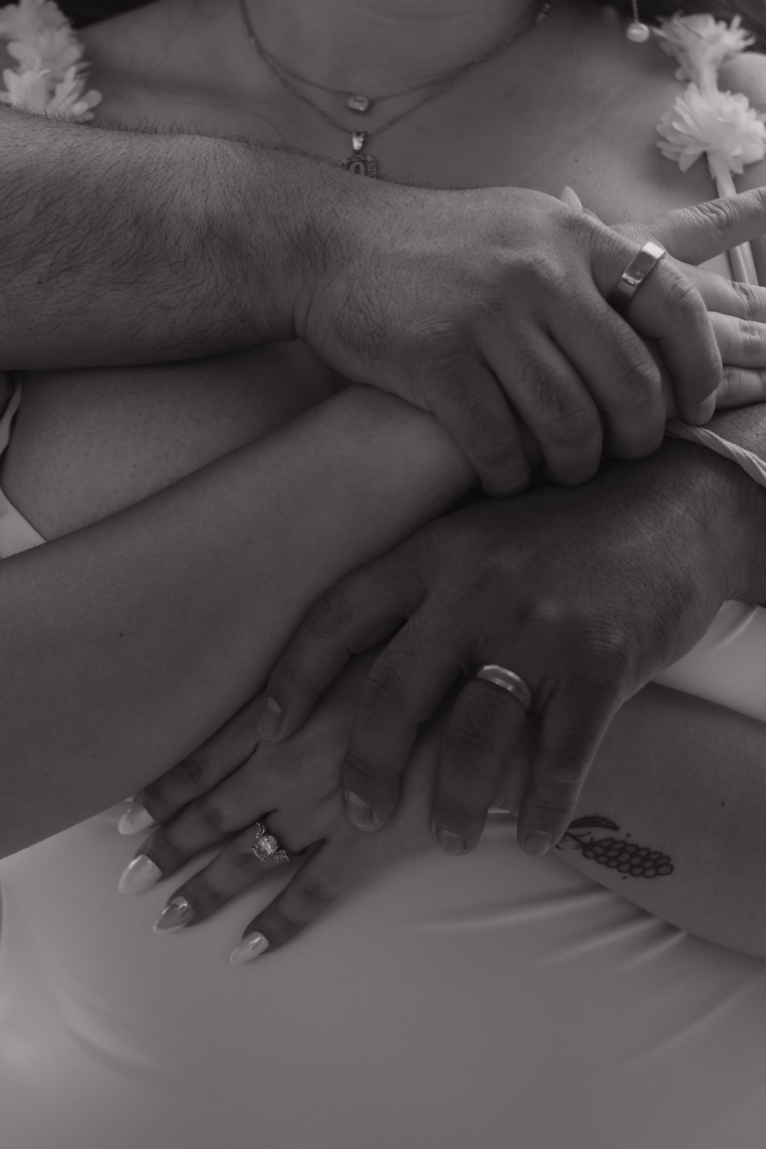 Black and white close-up of hands with wedding rings intertwined on a white surface.