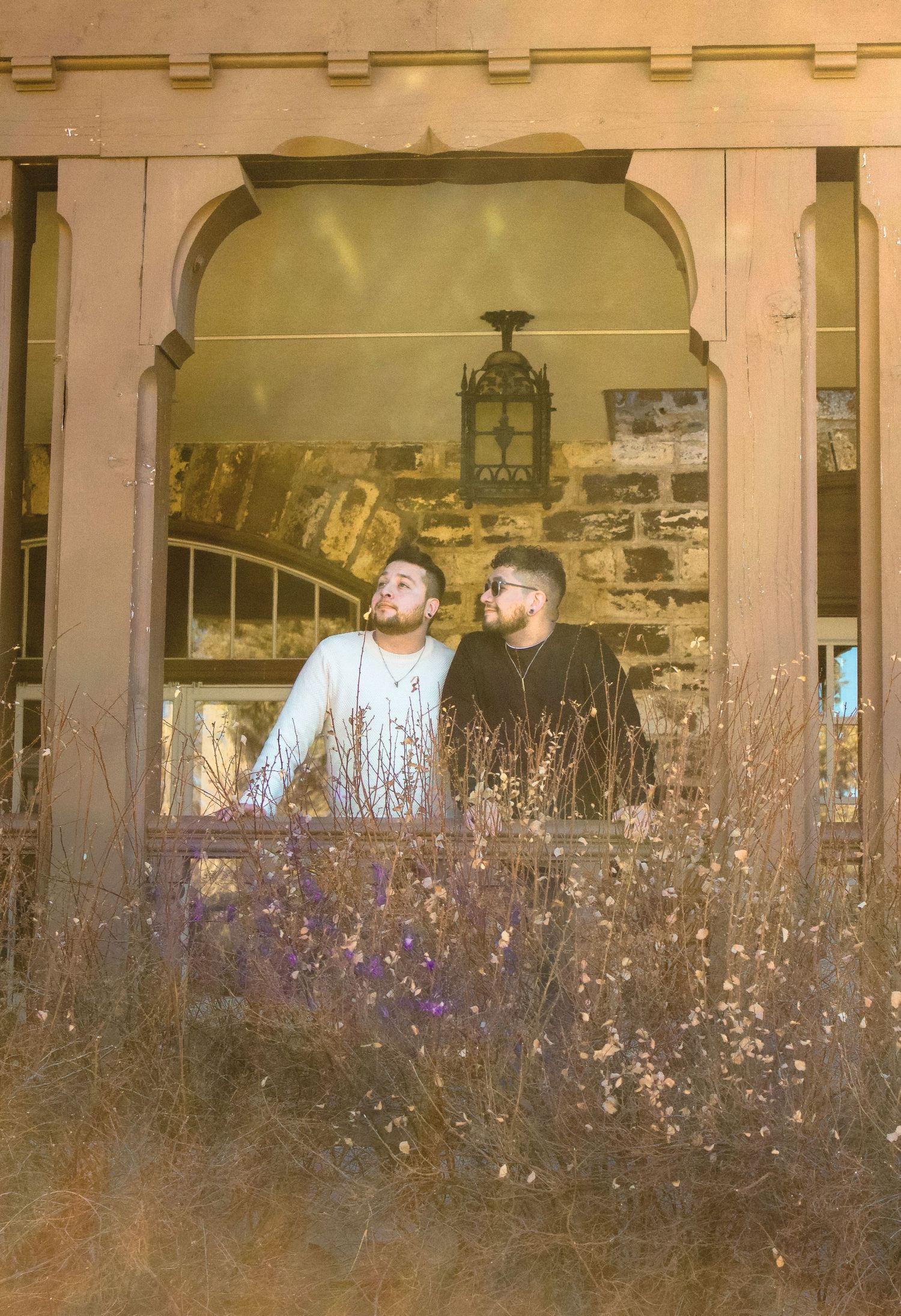 A romantic couple framed by an archway with dried flowers in the foreground.