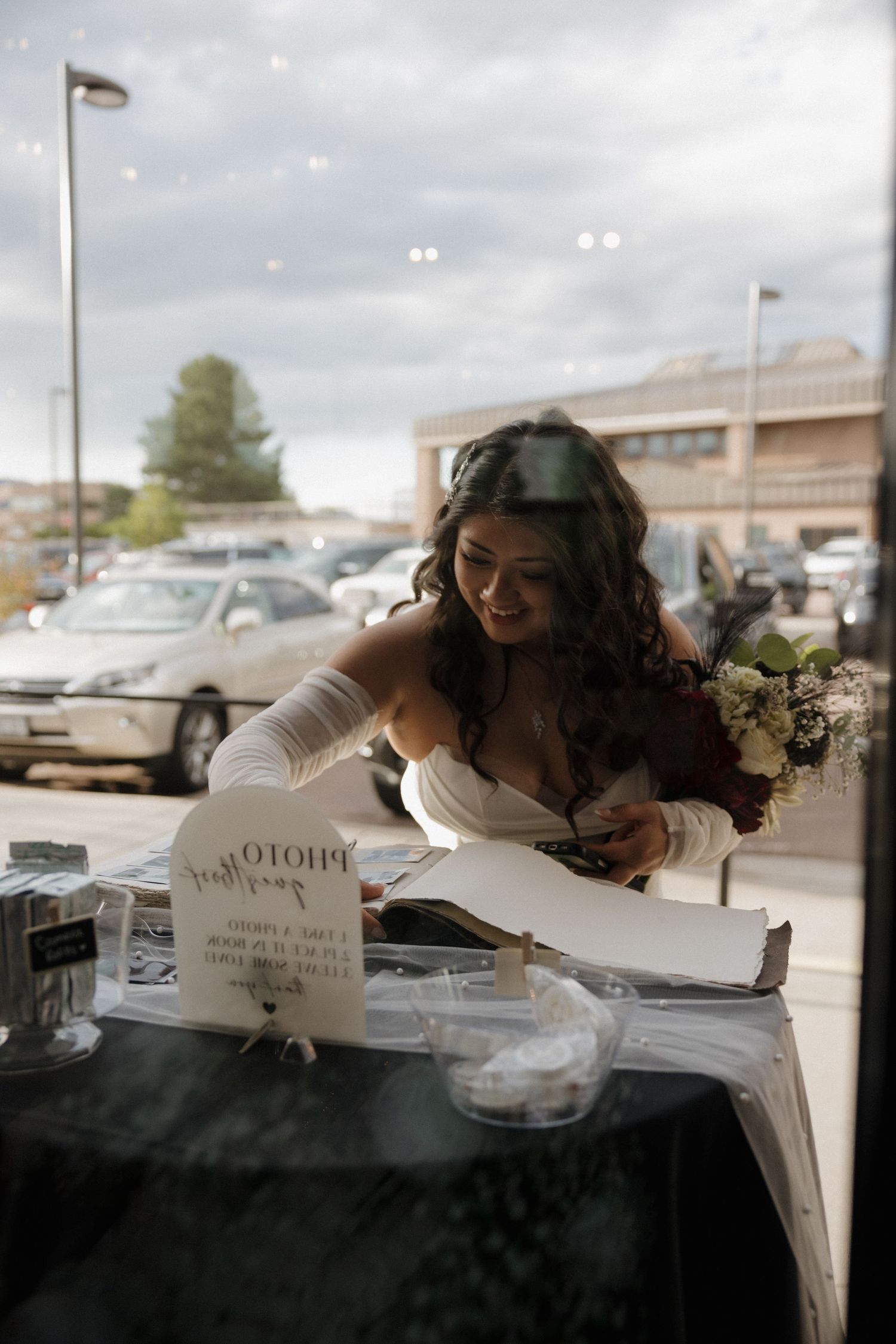 Beautiful bride in white gown with gloves reviews photo guest book at wedding reception table.