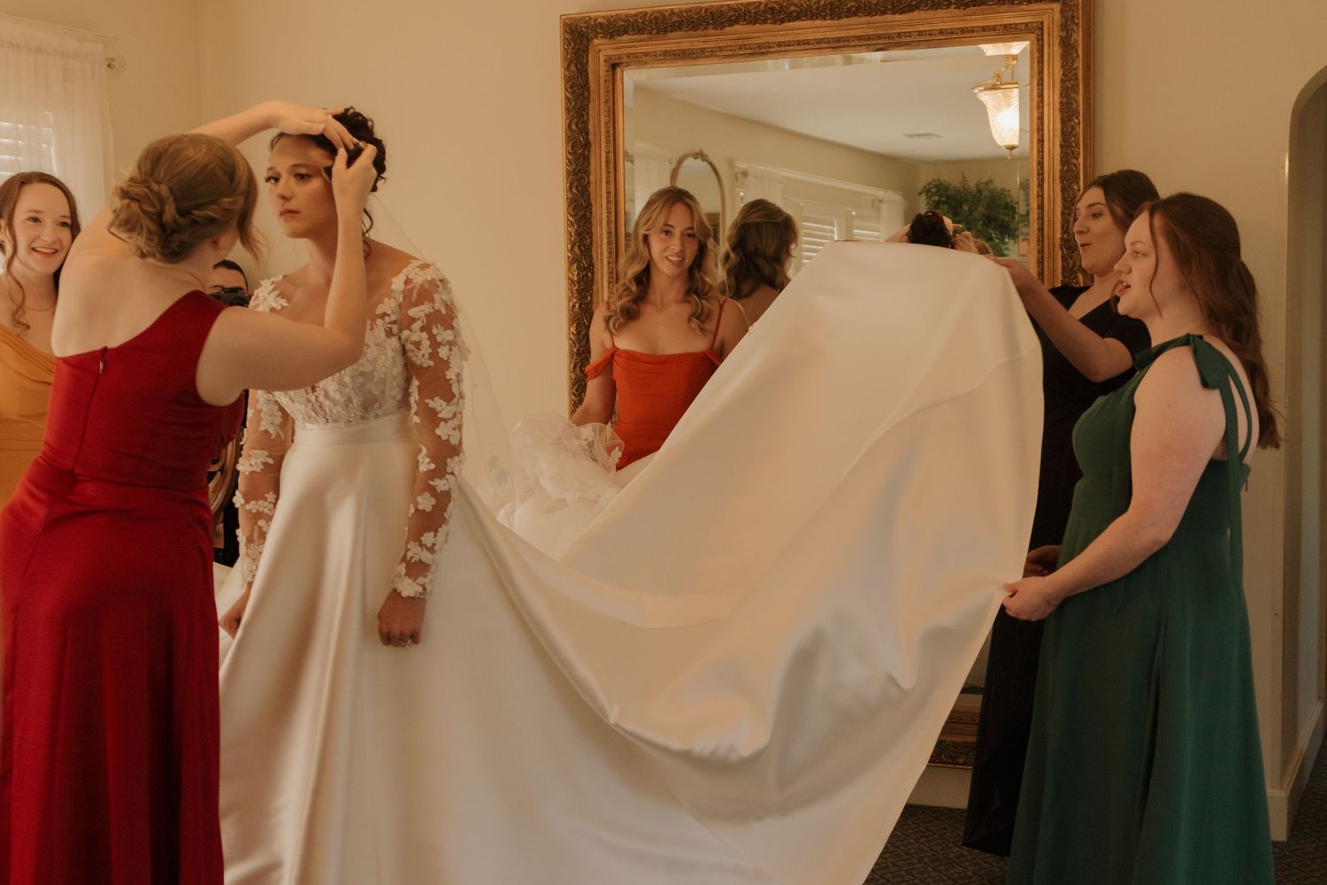 Wedding party gathered in a room with bridesmaids in burgundy and green dresses.