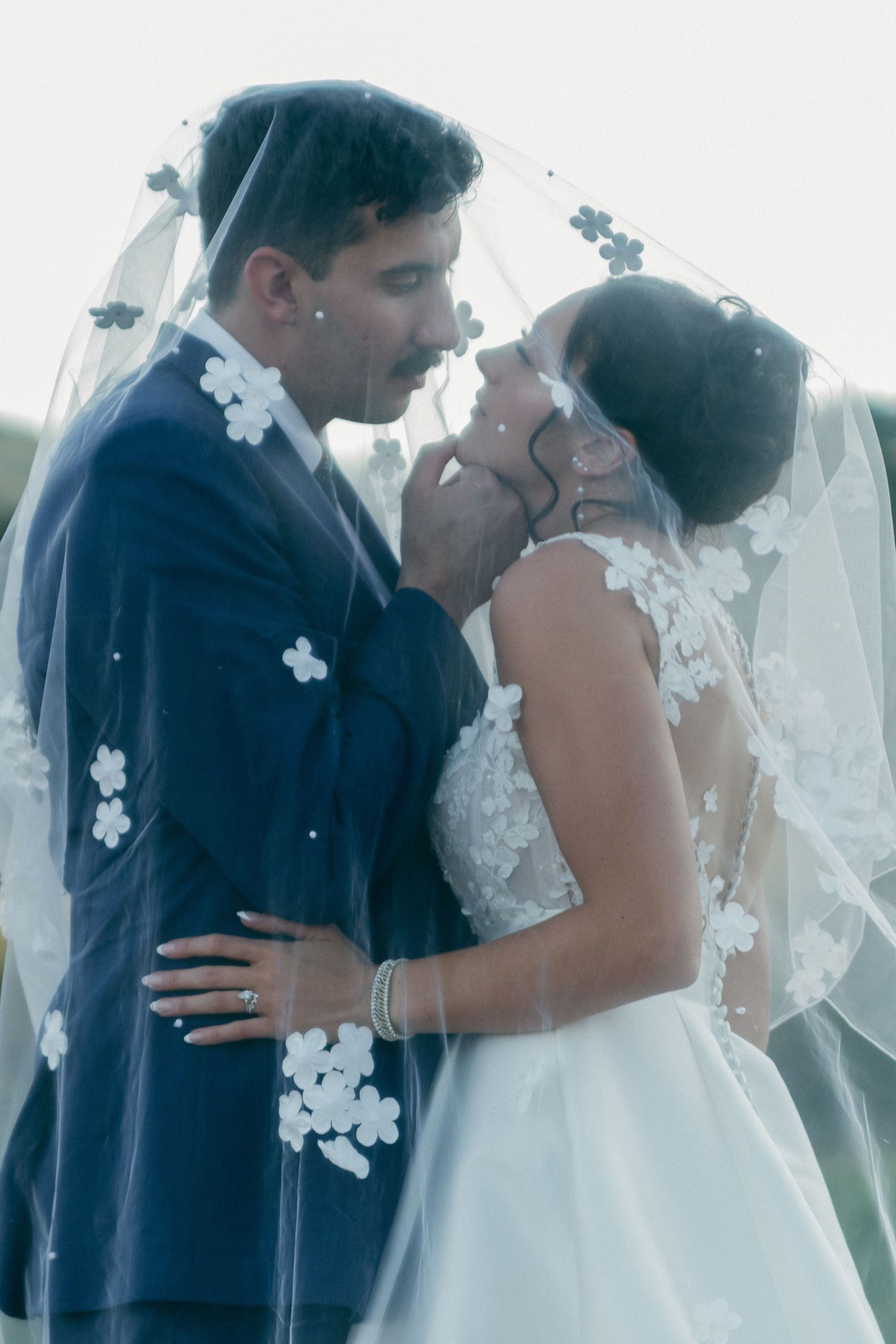 Romantic first kiss scene under delicate lace veil at outdoor wedding ceremony.