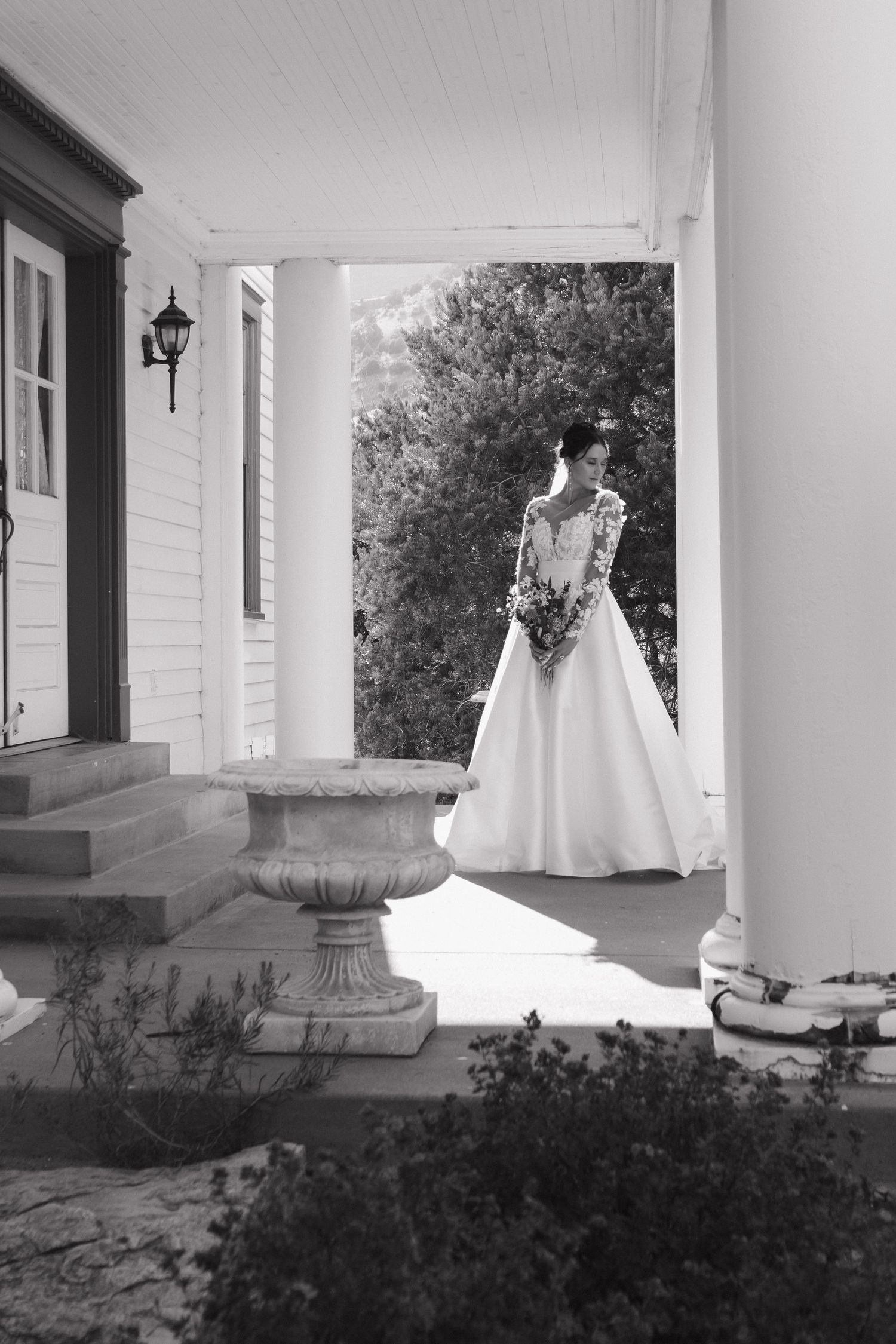 A classic black and white photo of a wedding dress on display on a white columned porch.
