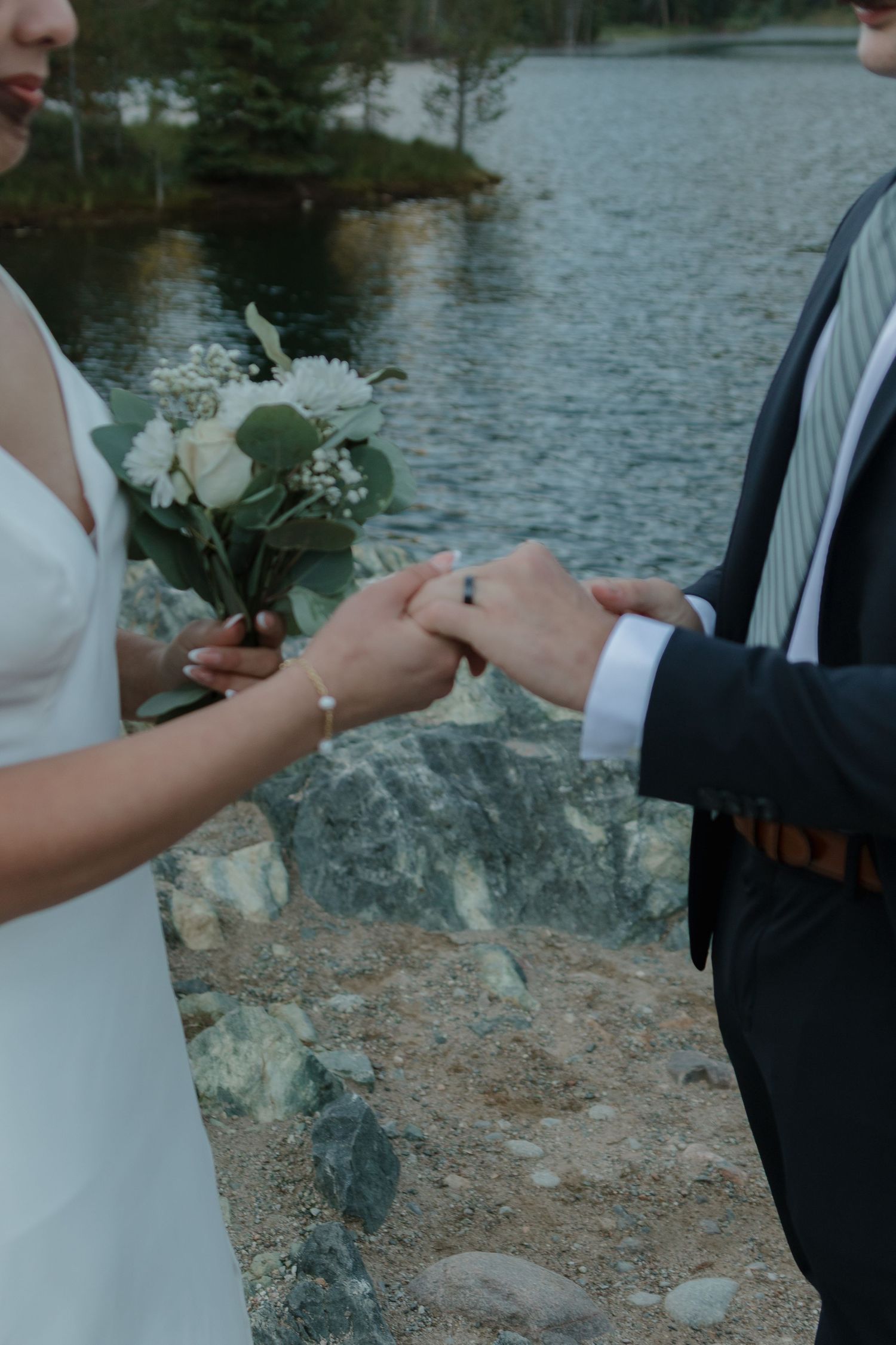 Newlyweds exchange rings during a lakeside ceremony on rugged rocks.