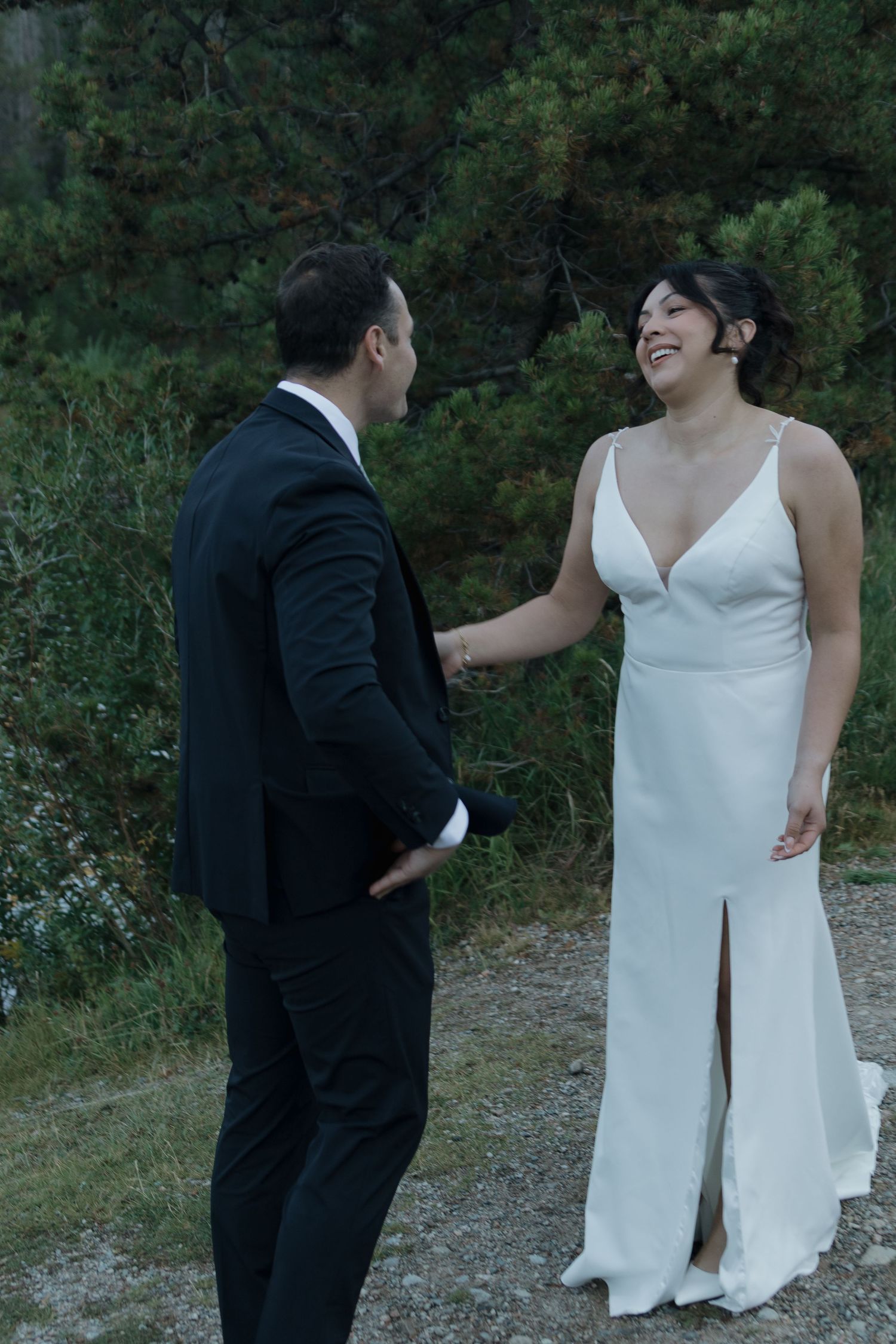 A couple shares a joyful moment on a forest path during their wedding photo session.