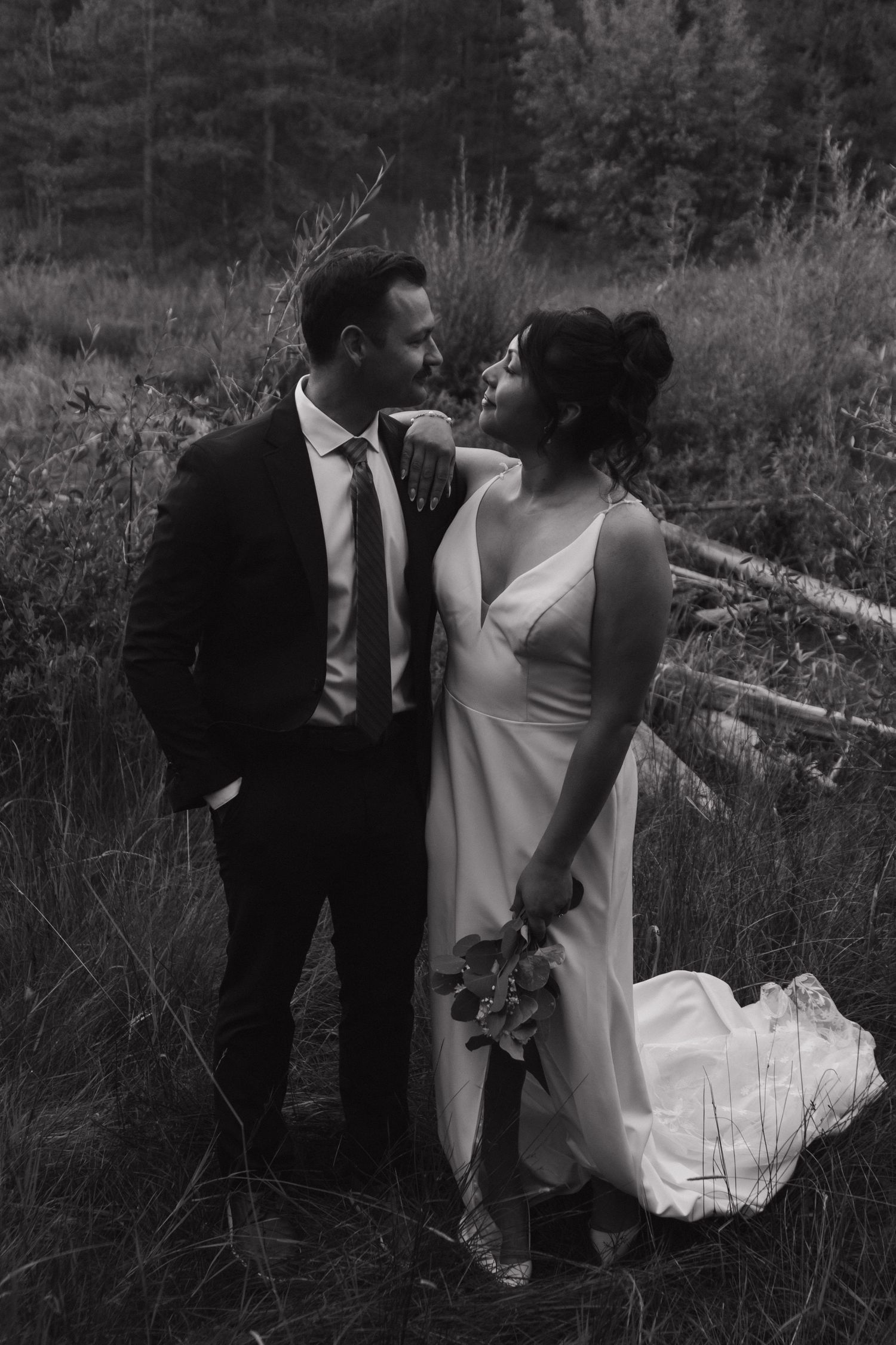 Black and white wedding photo showing couple in romantic pose among tall grass.