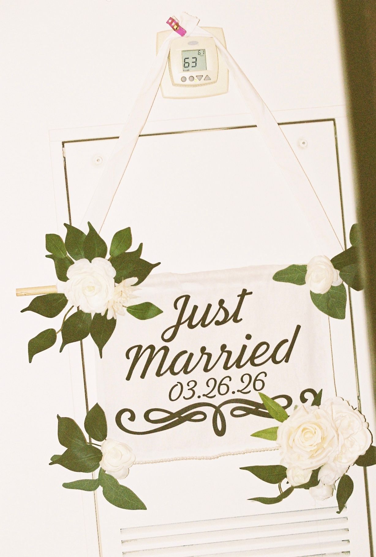 Just Married 03.26.26 sign decorated with white roses and green leaves on white wall.