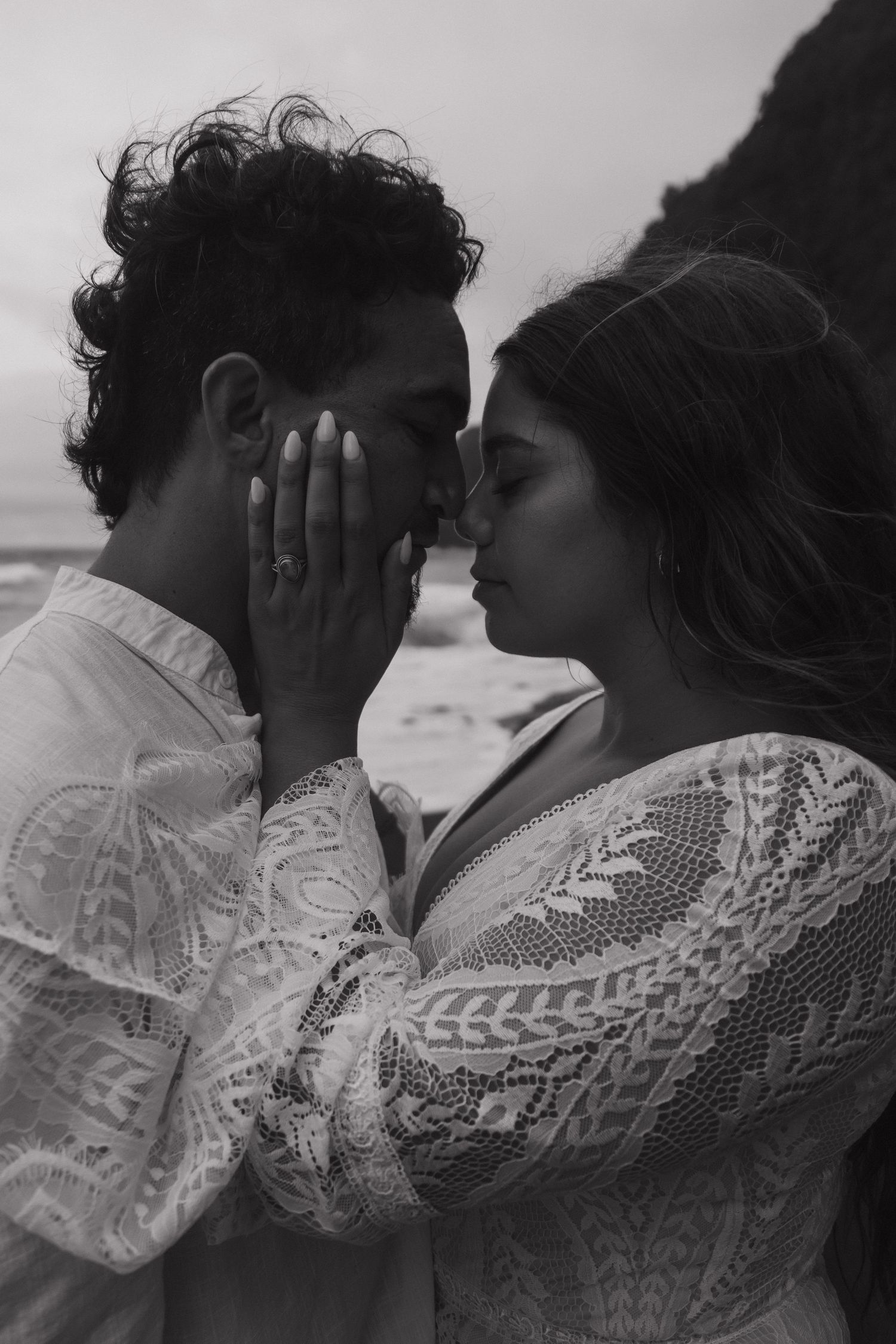 Intimate black and white close-up of bride and groom nearly kissing on a moody beach setting.