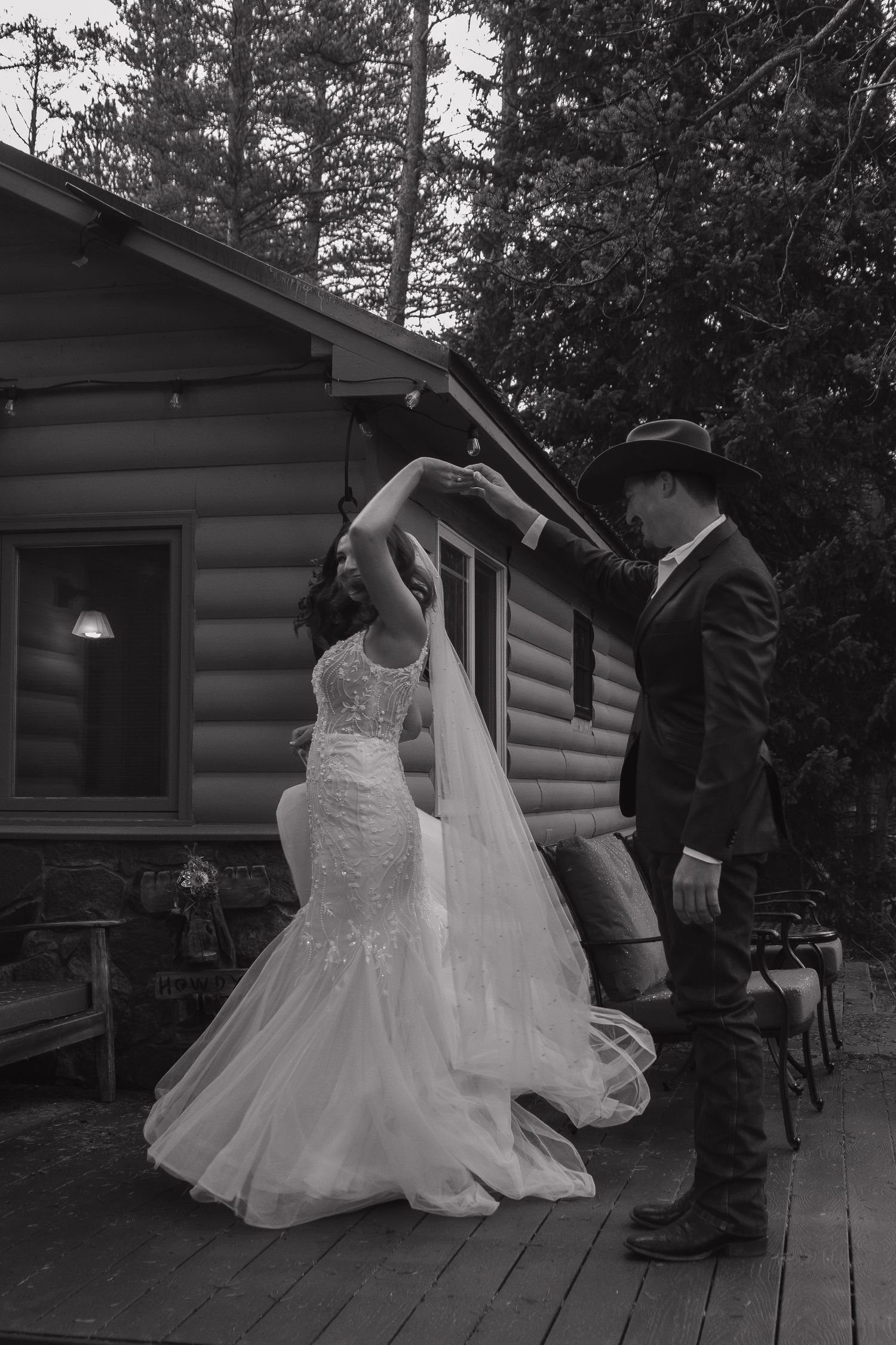 A couple shares a romantic moment on a rustic cabin deck during their black and white wedding photoshoot.