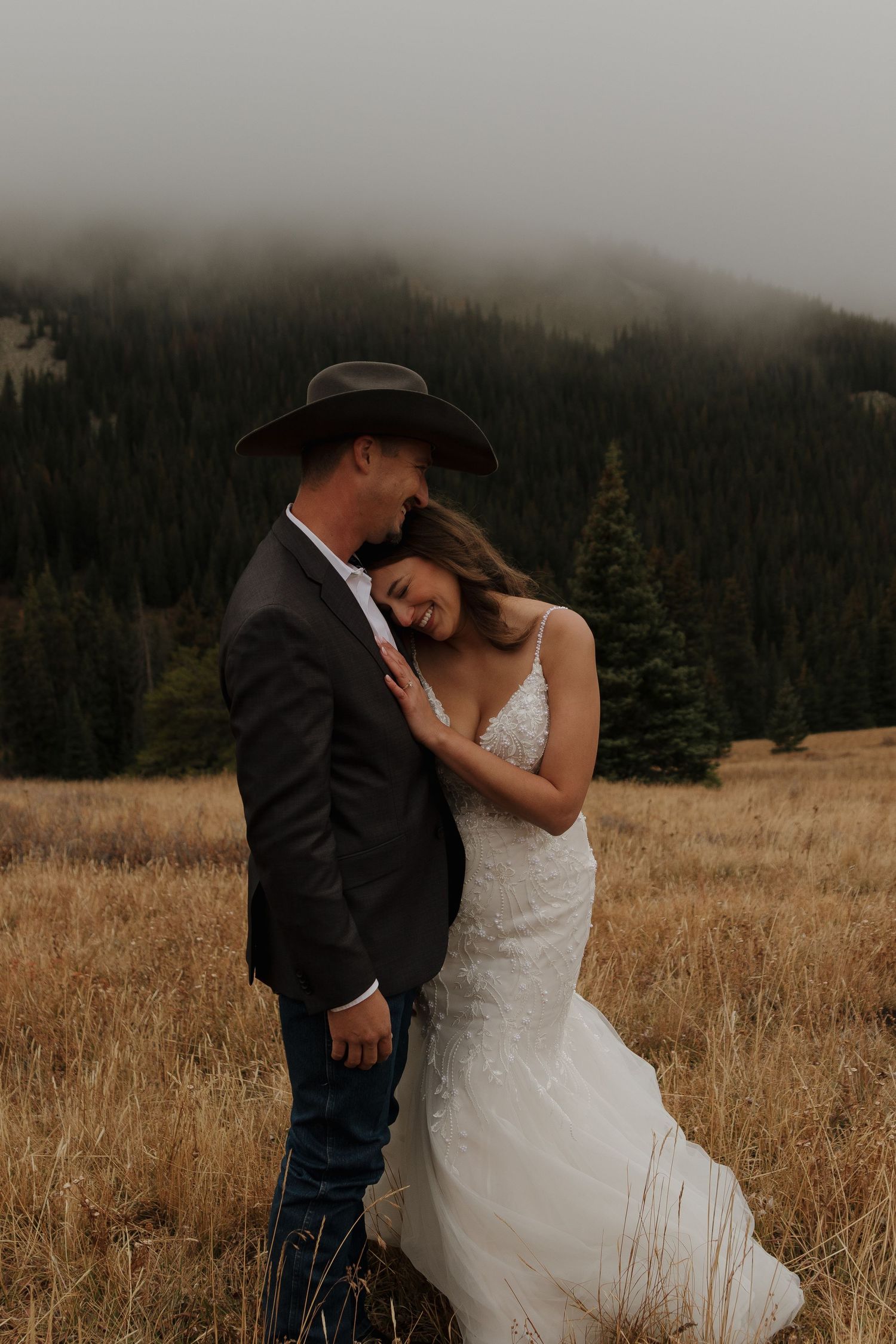 A romantic wedding portrait in a mountain meadow with misty peaks in the background.