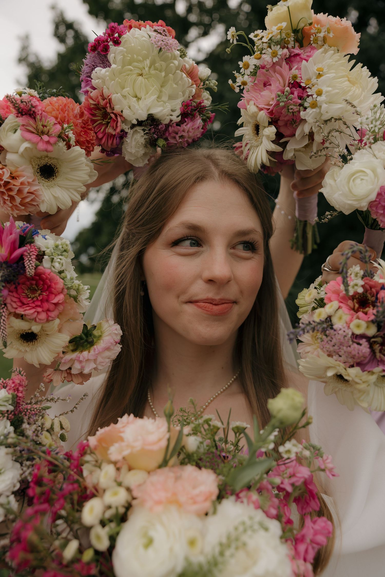 Smiling bride surrounded by colorful pink and white floral bouquets on her wedding day.