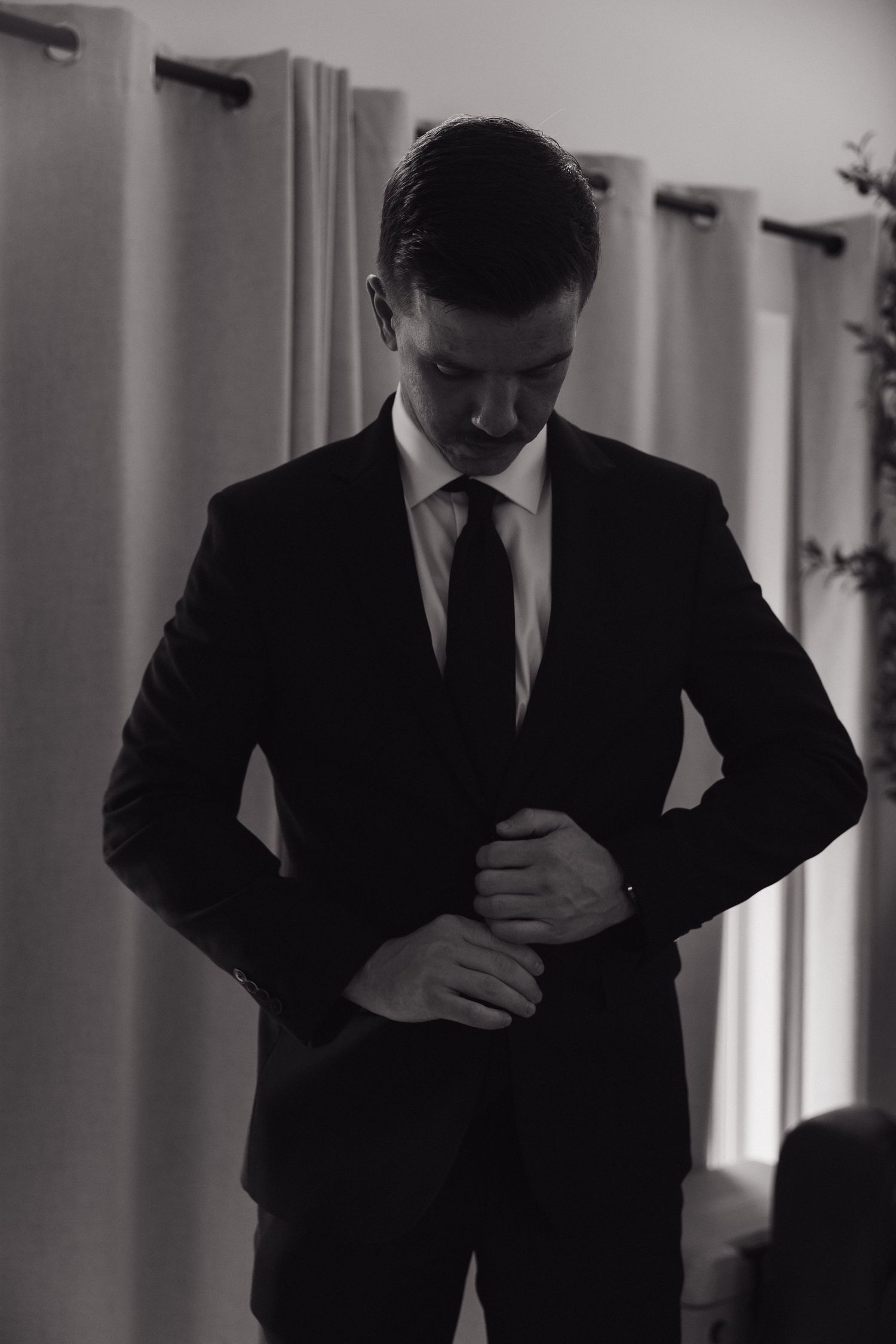 Groom in a black suit adjusting his jacket before the wedding ceremony.