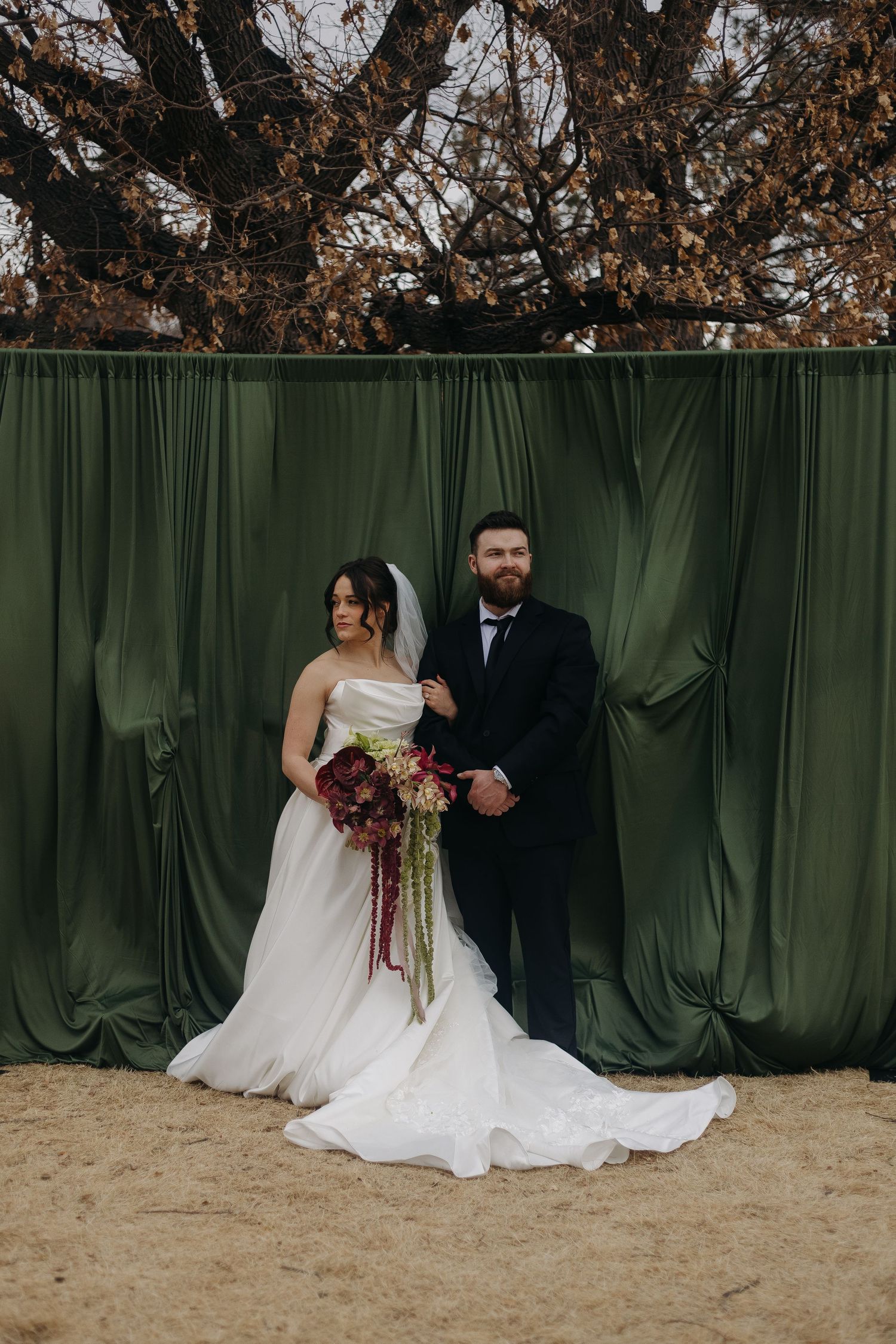 A bride and groom pose together against an emerald green velvet backdrop during their wedding photoshoot.