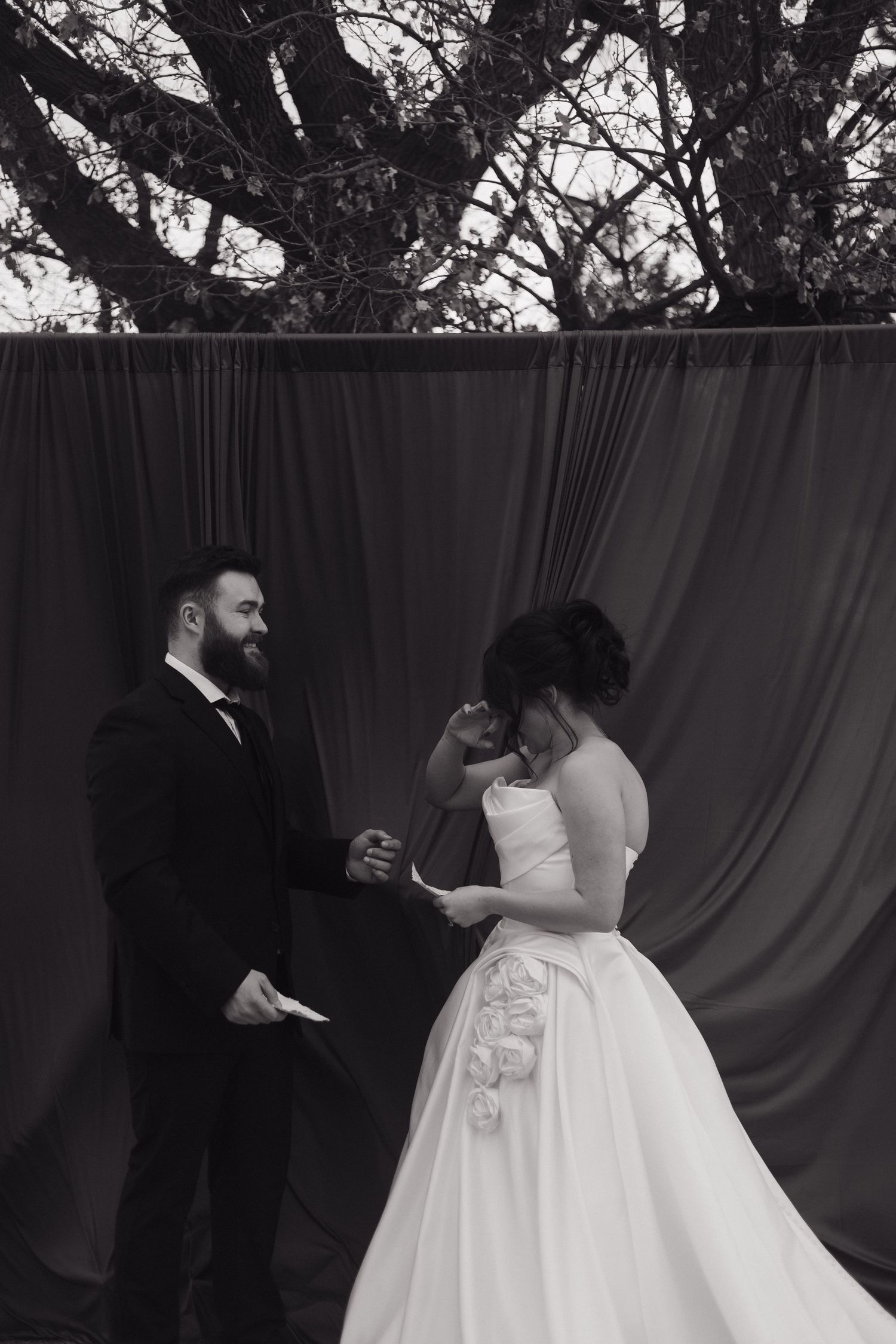 A couple in wedding attire dances together against a backdrop of trees.