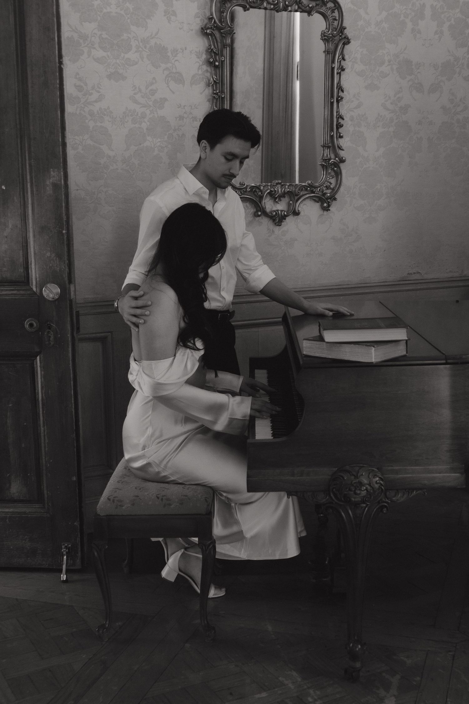 Artistic black and white photo of couple at piano in elegant vintage room.