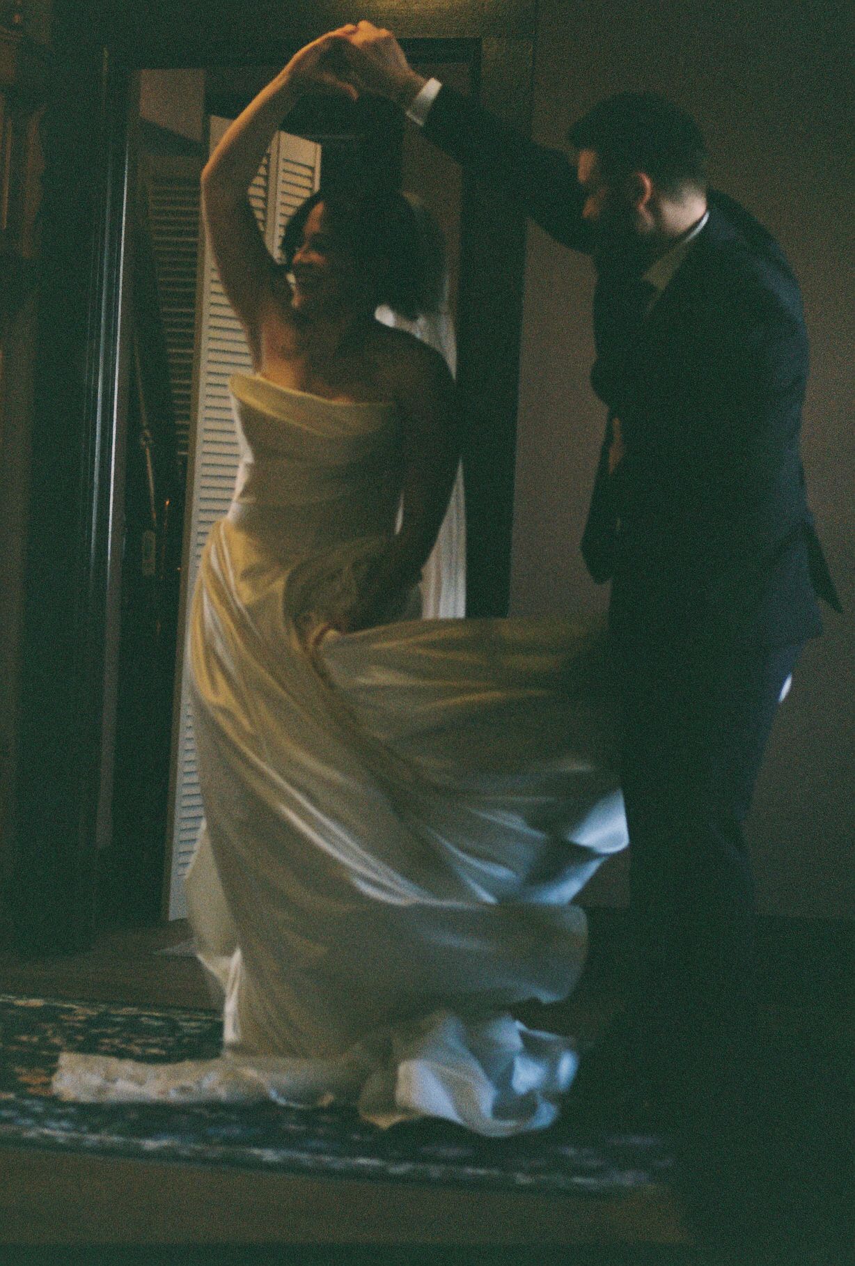 Atmospheric low-light wedding scene with dramatic shadows and flowing white fabric.