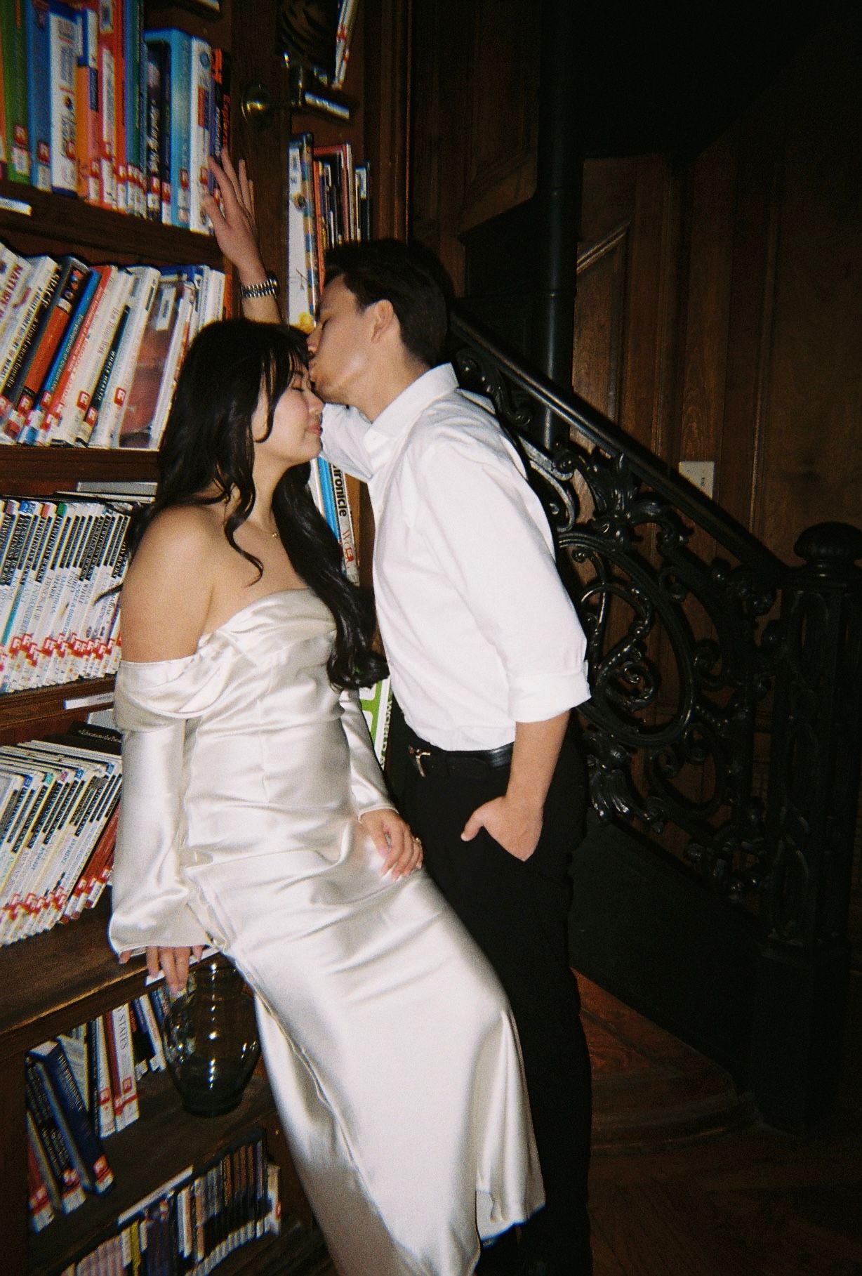 A couple shares a dance moment between library bookshelves in moody lighting.