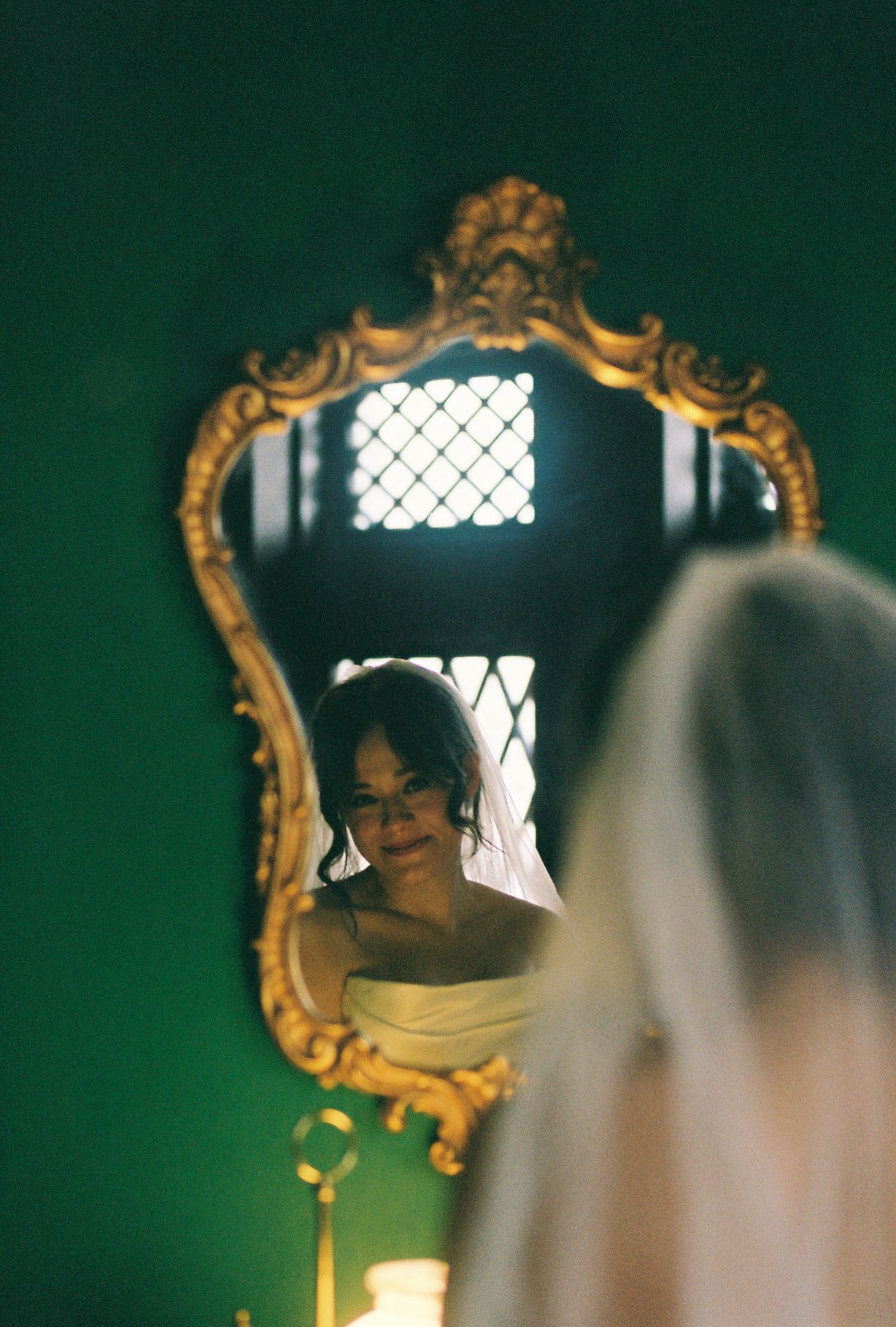 Reflection in an ornate gold mirror with emerald green walls and soft lighting.