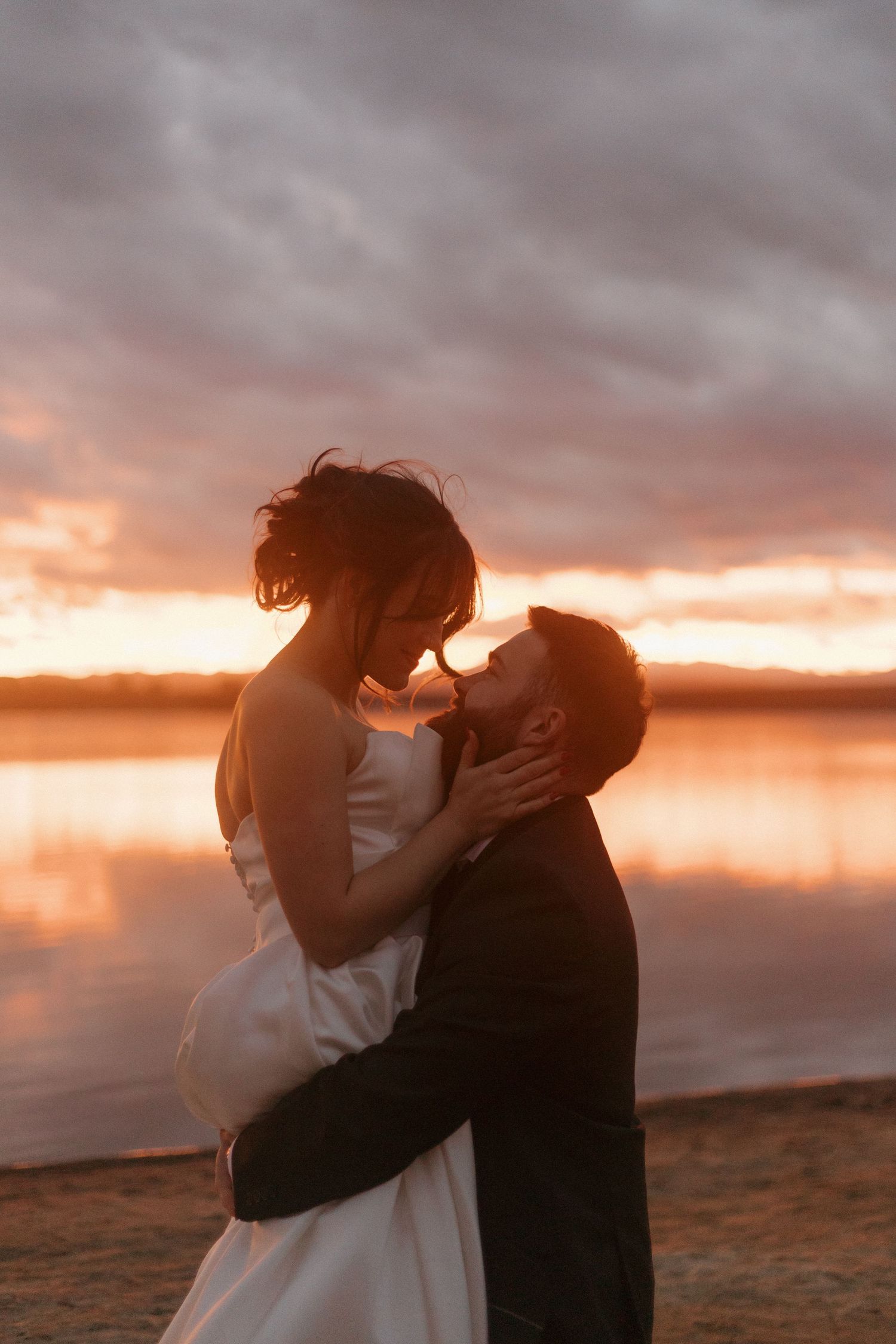 Newlyweds share an intimate moment against a dramatic sunset sky on their wedding day.