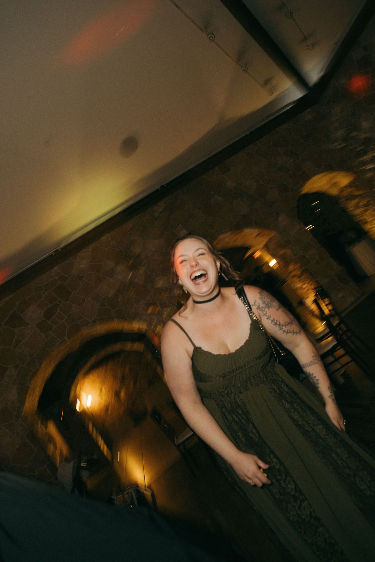Joyful wedding guest in olive dress laughs on the dance floor during evening reception celebration.