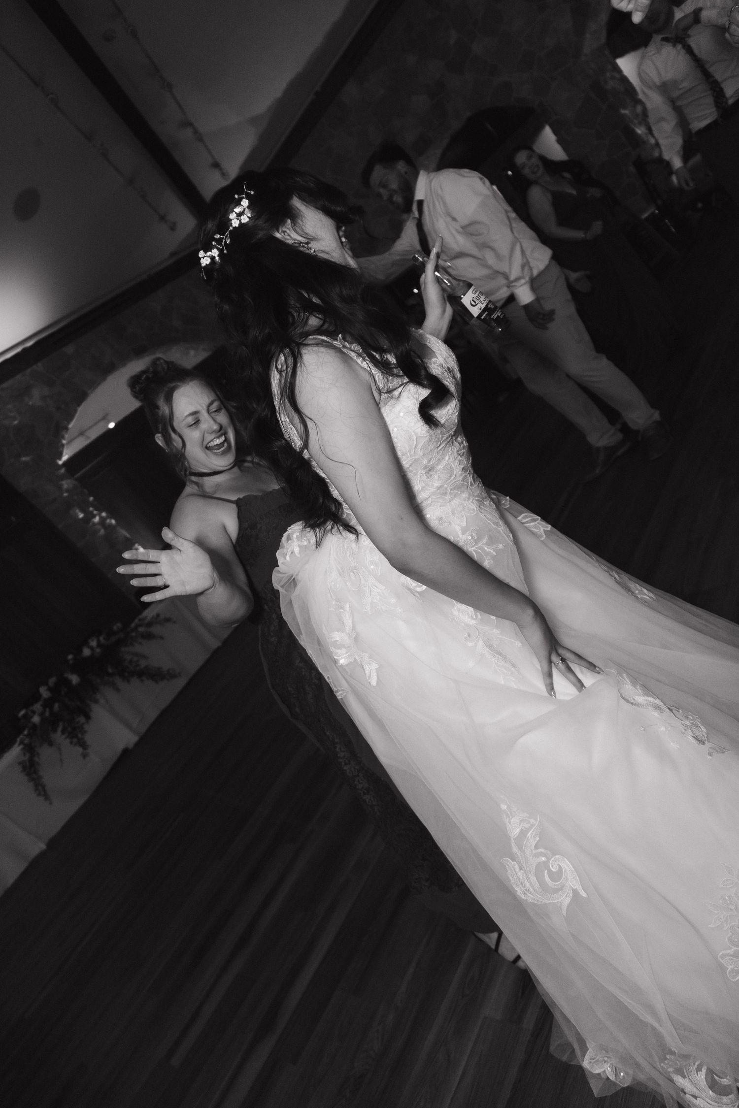 Bride in lace gown dancing and laughing with a guest on the wedding reception dance floor.