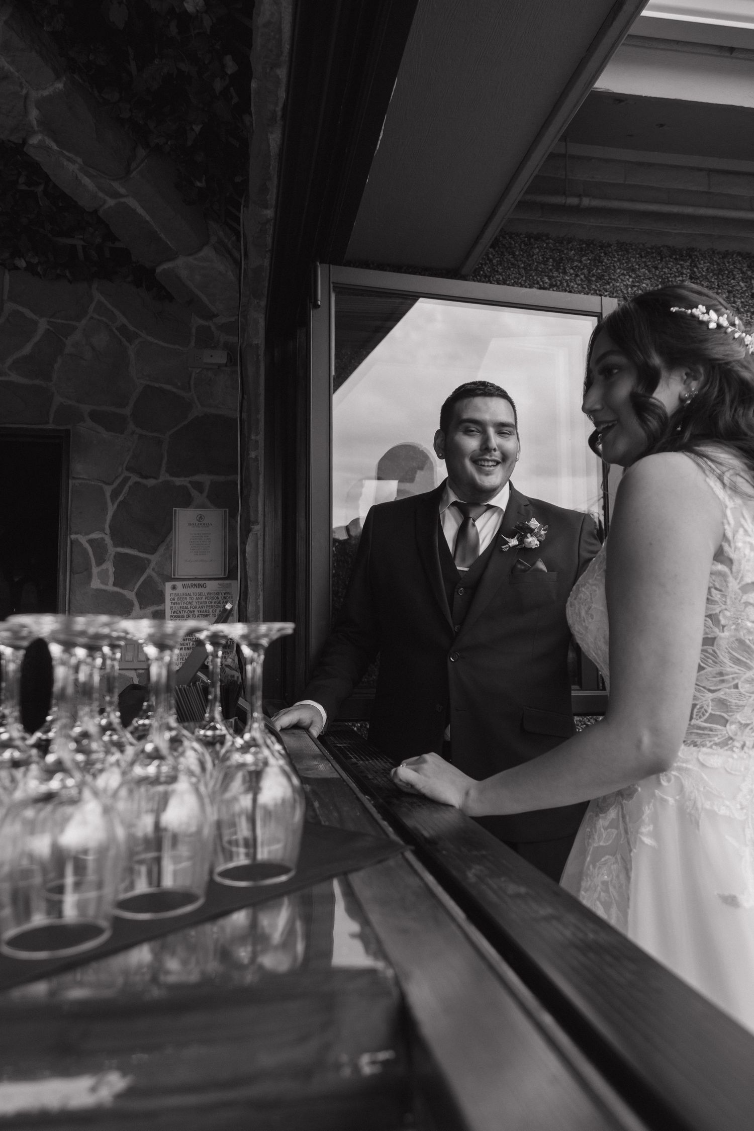 Bride and groom share a joyful moment at the bar in this black and white wedding photo.