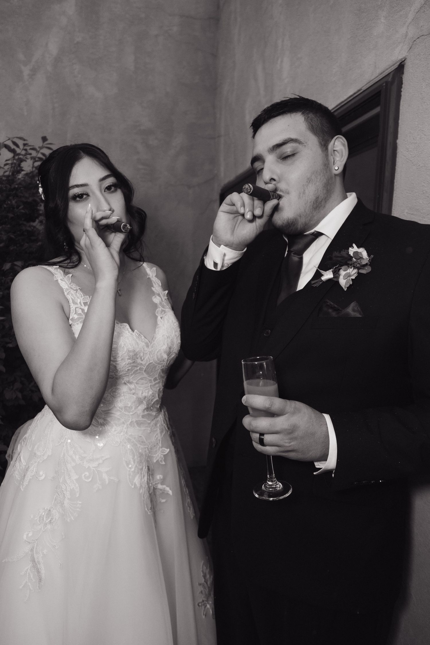 Bride and groom smoking cigars and holding champagne at their wedding reception in black and white.