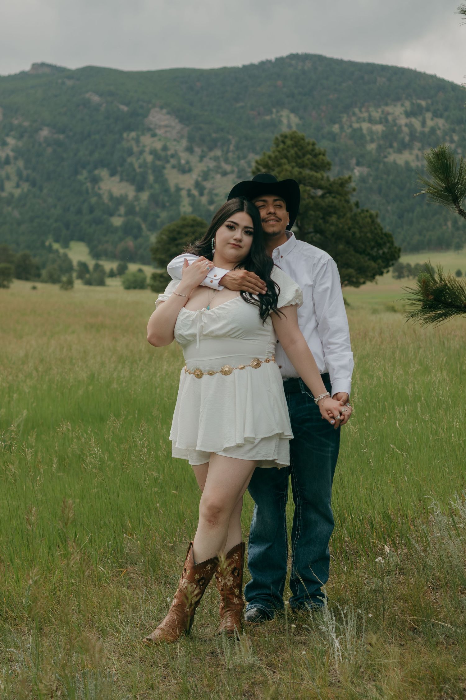 A romantic photoshoot in a mountain meadow featuring western style clothing and natural scenery.