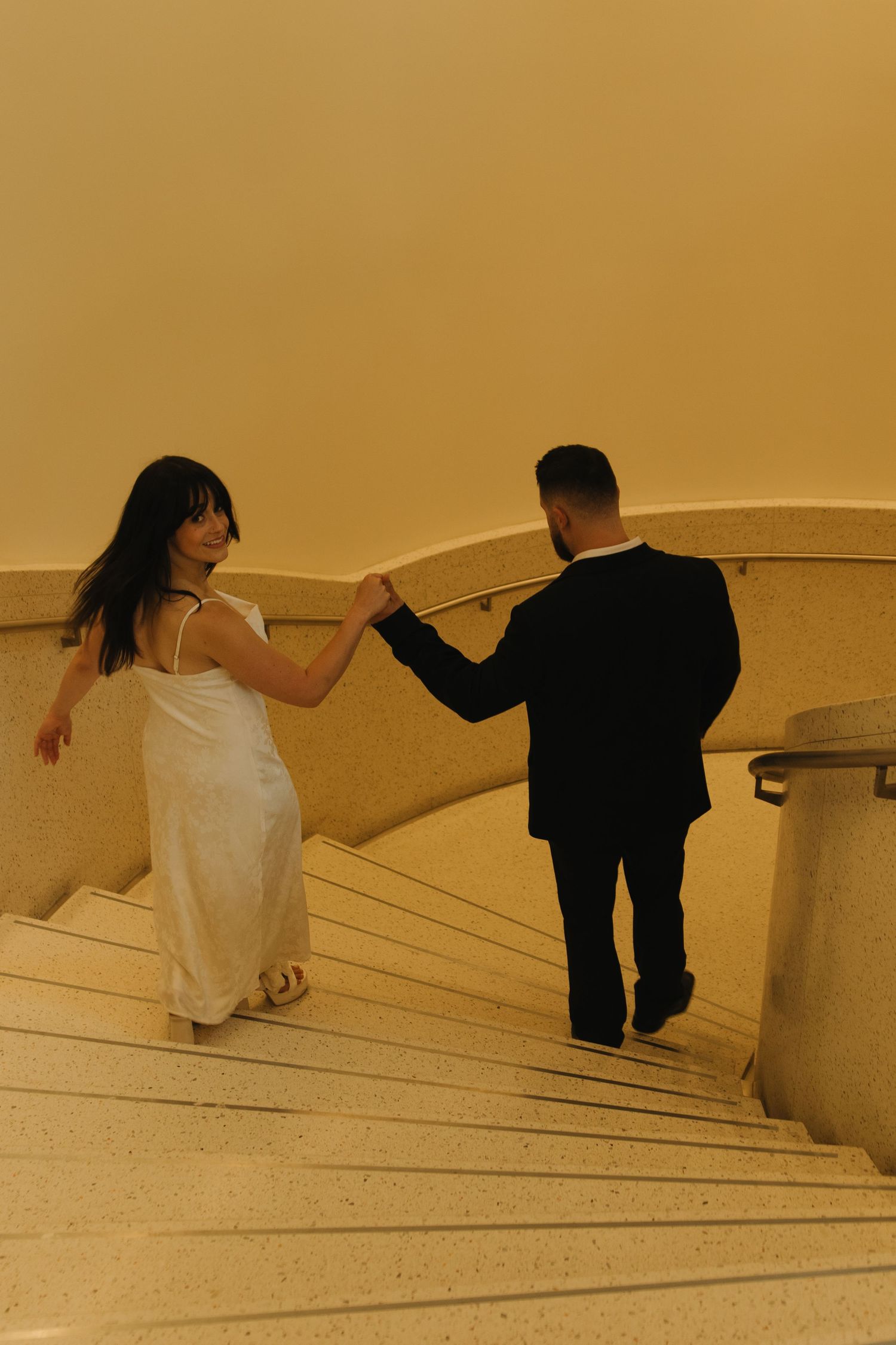 Couple descending white marble stairs in an artistic sequence of movement.