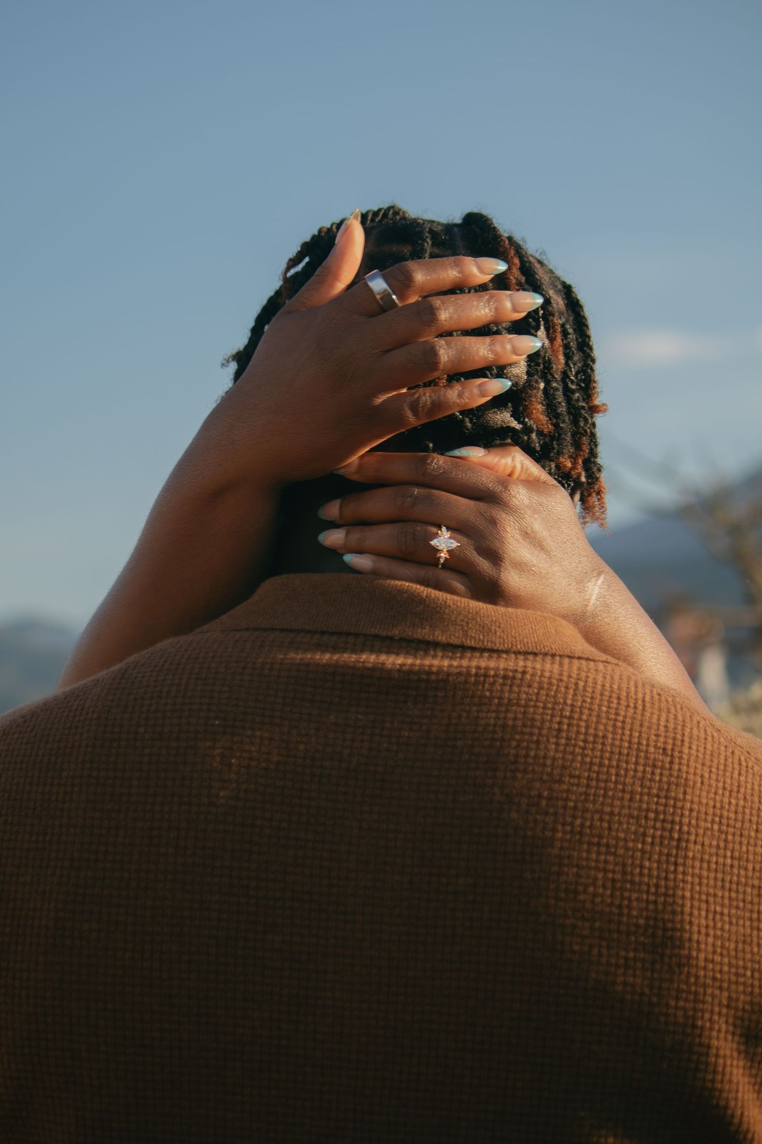 An intimate close-up shot showing hands resting gently on a brown textured surface against a blue sky.