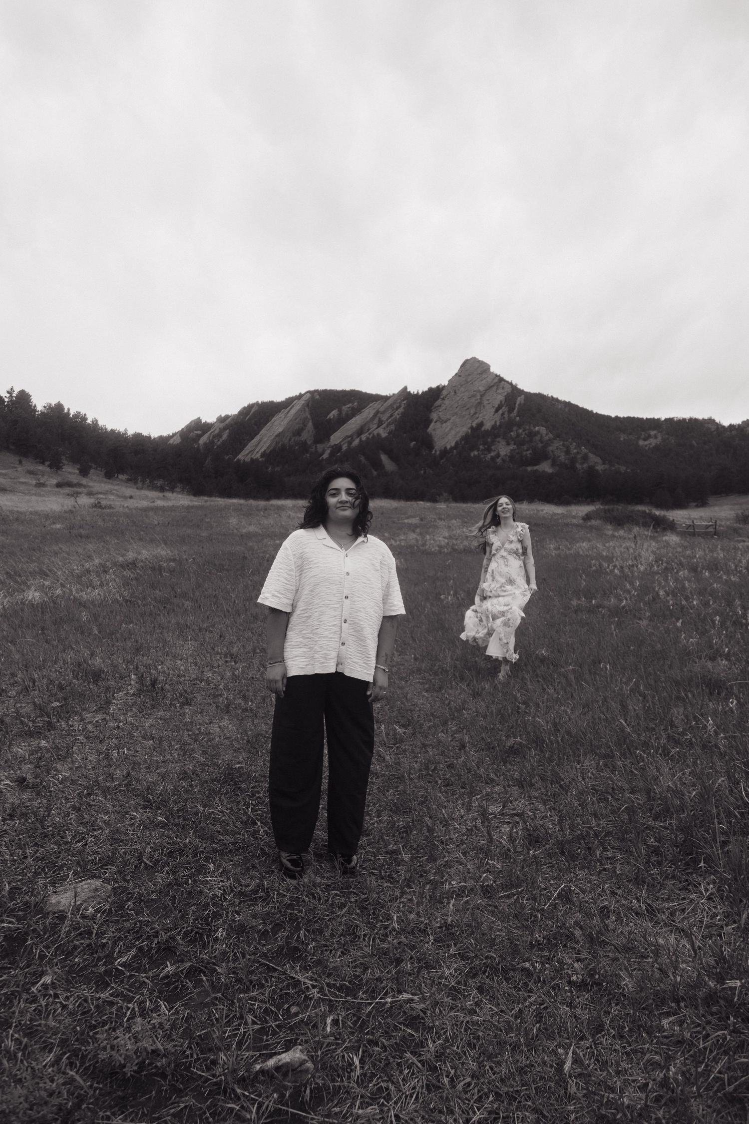 Black and white photo of two women posing in a wide open field with iconic Boulder Flatirons behind.