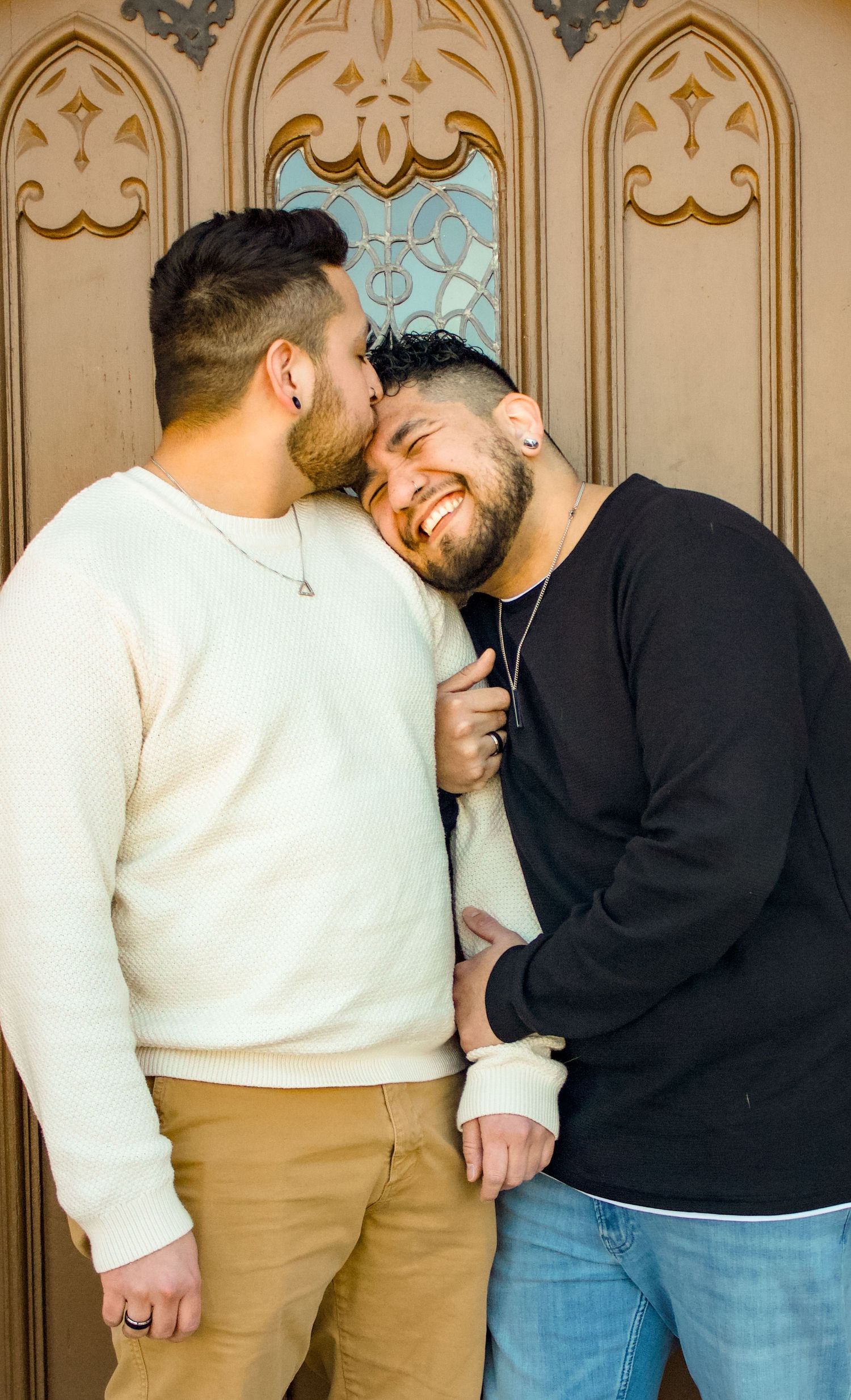 A couple embracing and laughing together in front of a decorative Gothic-style door.
