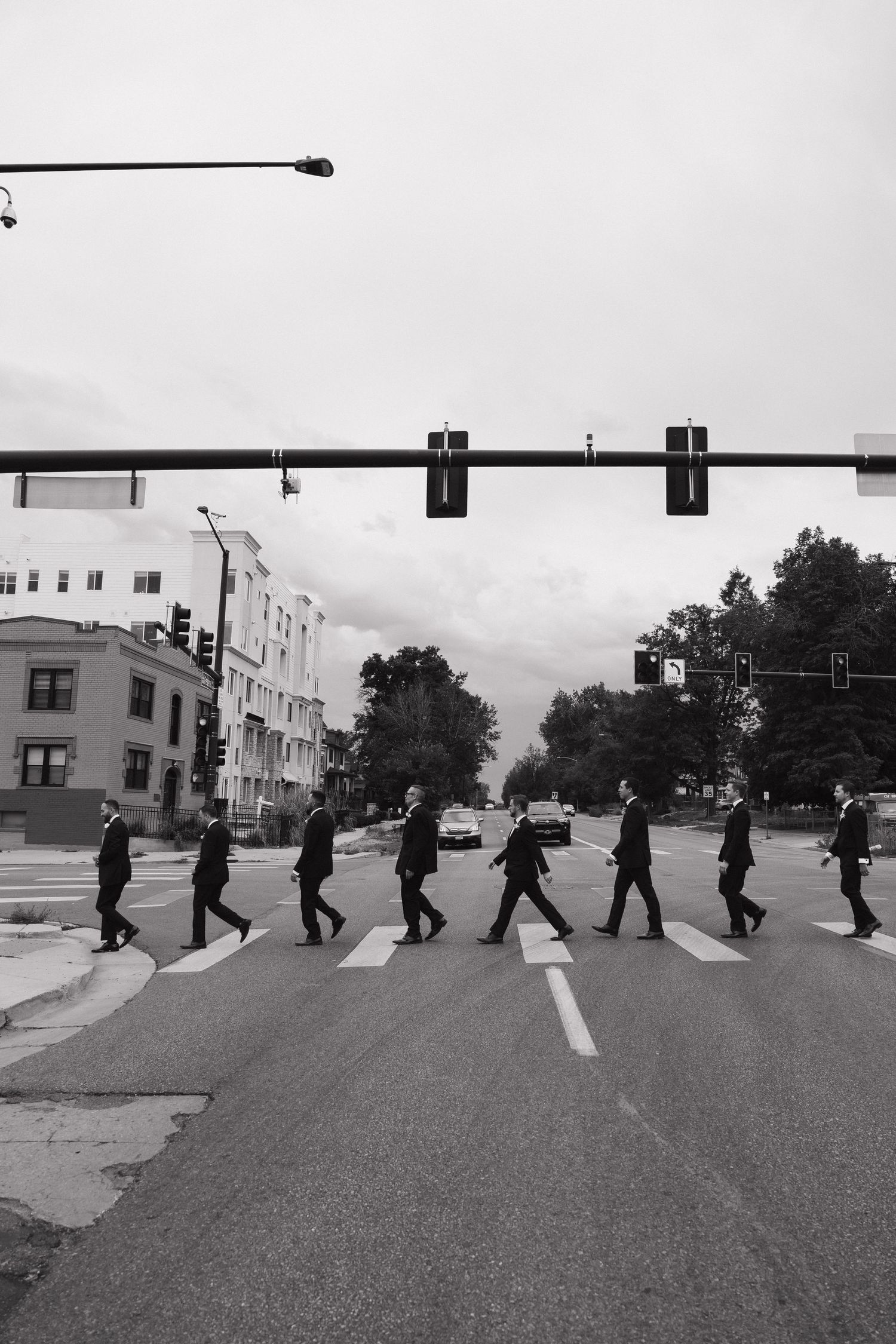 Groomsmen in black suits cross a zebra crossing in black and white photo, inspired by Abbey Road.