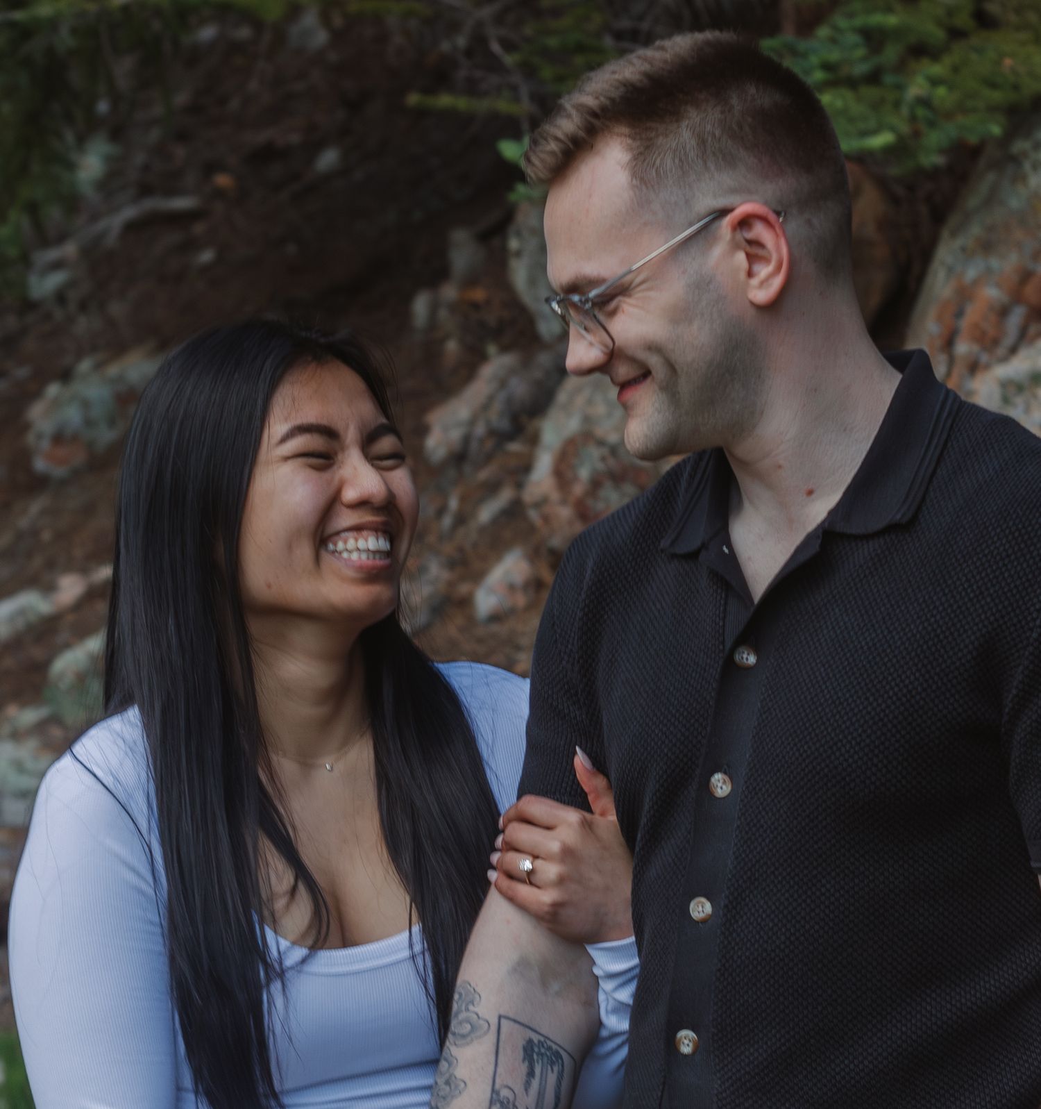 A couple shares a joyful intimate moment while standing against a rocky forest backdrop.