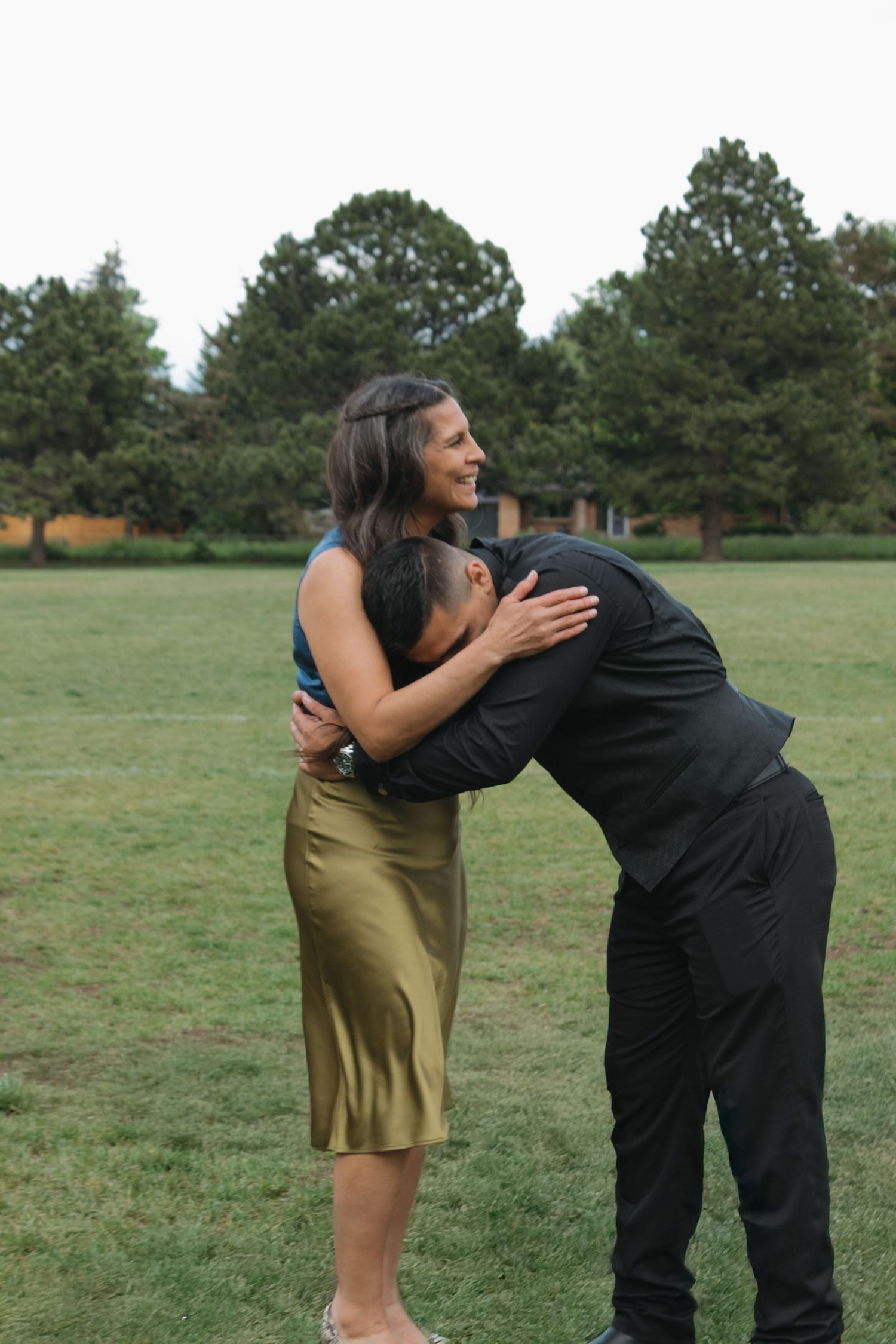 Couple in formal attire sharing a playful moment on grassy field.