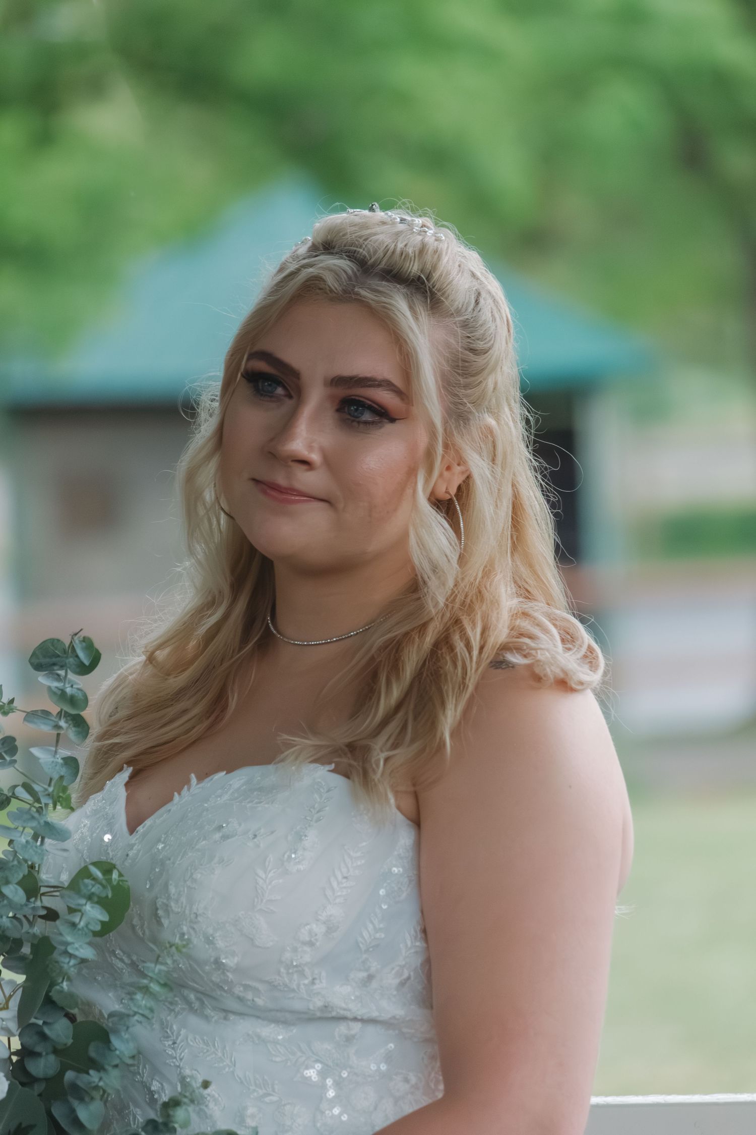 A person in a sparkly white wedding dress poses with eucalyptus bouquet in an outdoor setting.